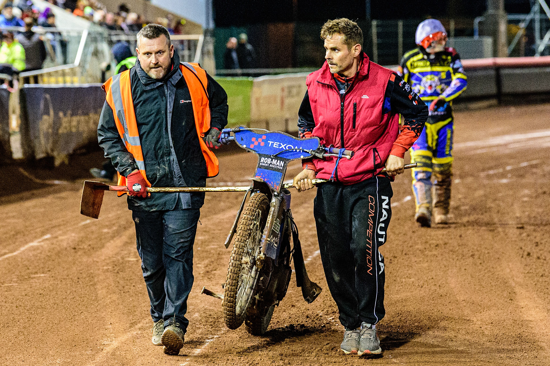 A Track staff member helps Tobiasz Musielak’s mechanic carry his damaged bike from the track after his crash during the SGB Premiership Grand Final 1st leg between Belle Vue Aces and Sheffield Tigers at the National Speedway Stadium, Manchester on Monday 10th October 2022. (Credit: Ian Charles | MI News)