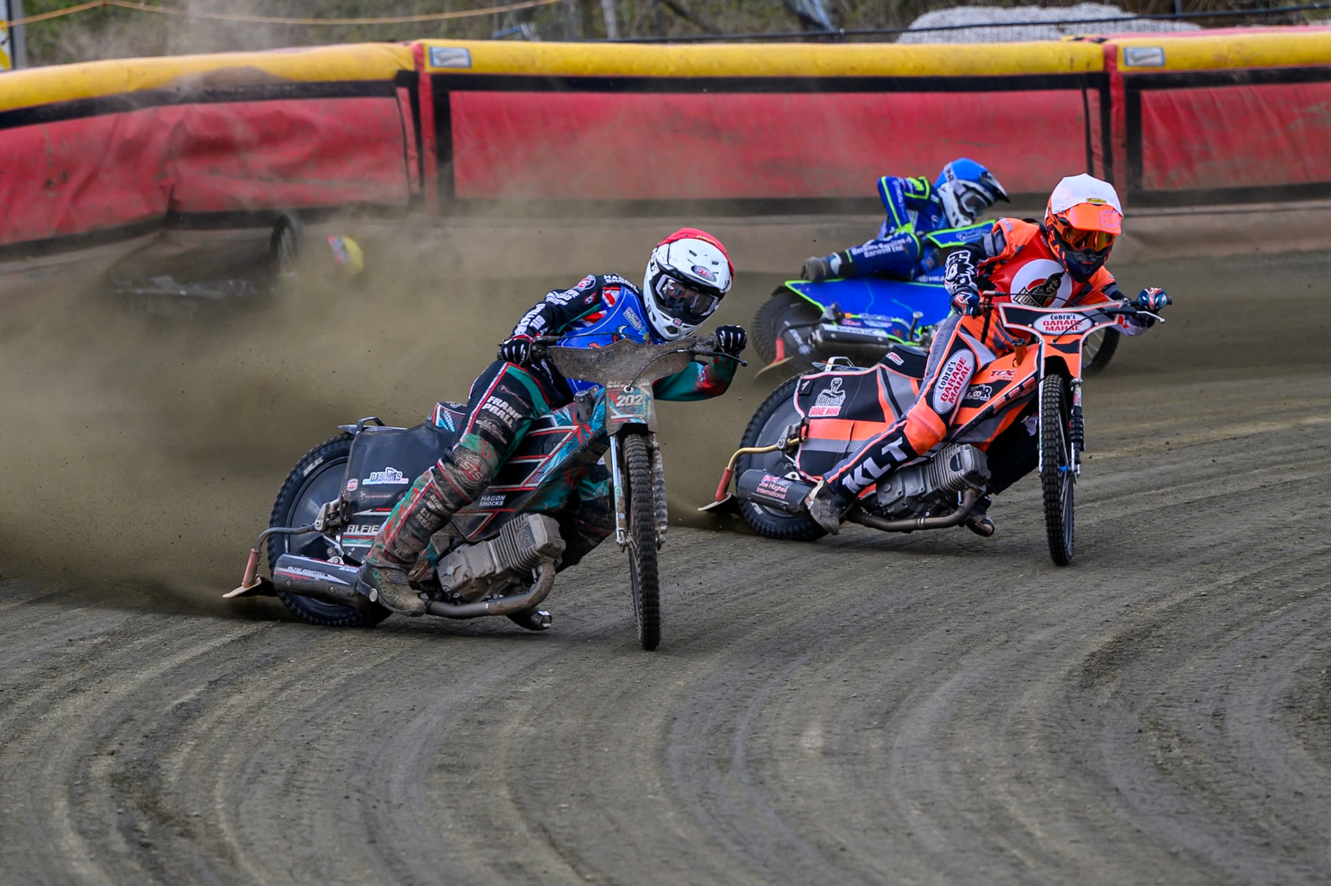 Alfie Bowtell of Buxton Bulls  in Red Connor Coles of NDL Nomads in White as Sam Woods of NDL Nomads  slides into the safety fence as Arran Butcher of Buxton Bulls  spins his machine during the  Challenge match between Buxton Bulls and NDL Nomads at Hi-Edge Speedway, Buxton on Sunday 19th April 2026. (Photo: Ian Charles | MI News)