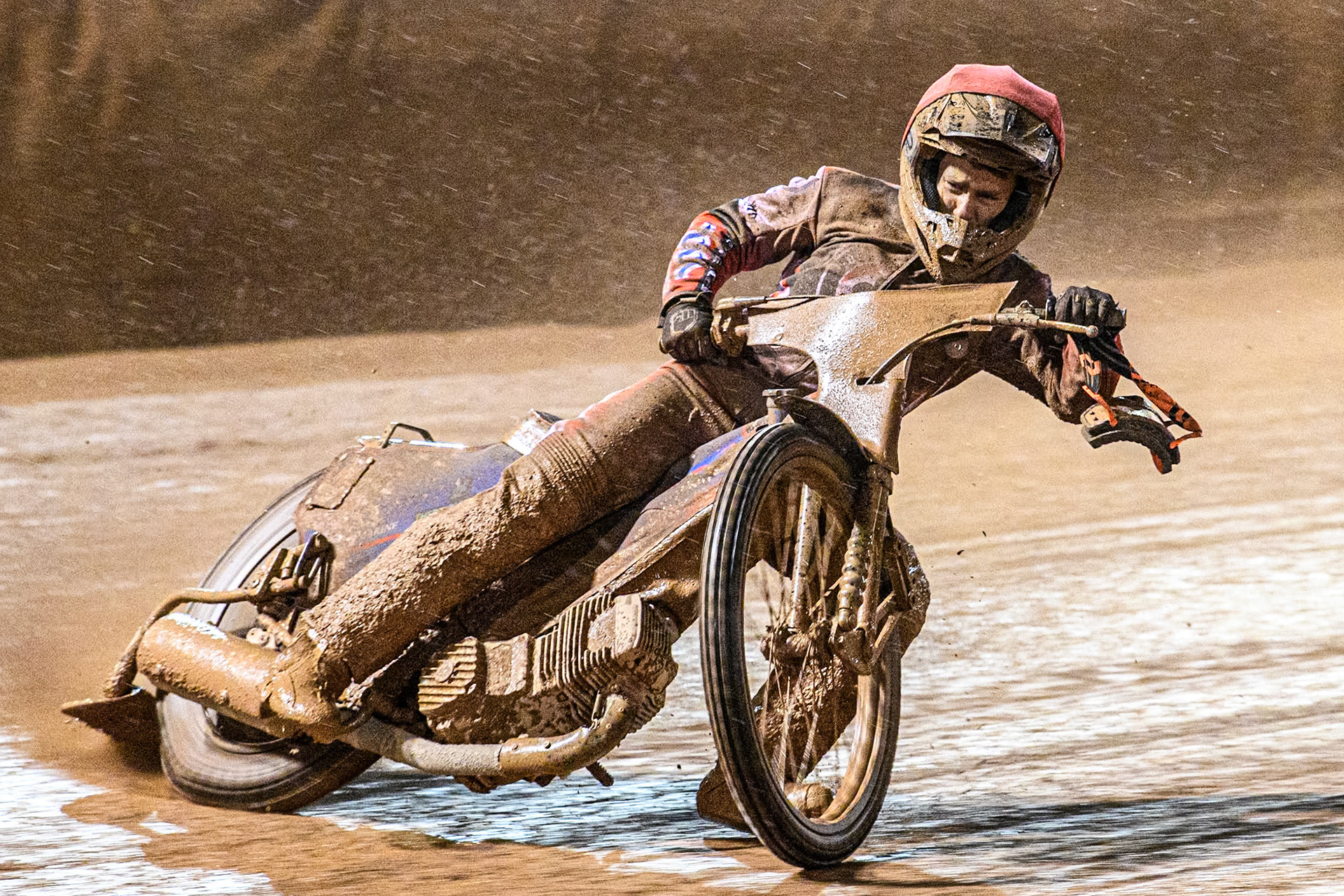 Ben Cook of Belle Vue Aces rides through the mud with his goggles on his left wrist after he couldn’t see where he was riding during the Rowe Motor Oil Premiership match between Belle Vue Aces and Leicester Lions at the National Speedway Stadium, Manchester on Saturday 6th April 2024. (Photo: Ian Charles | MI News)