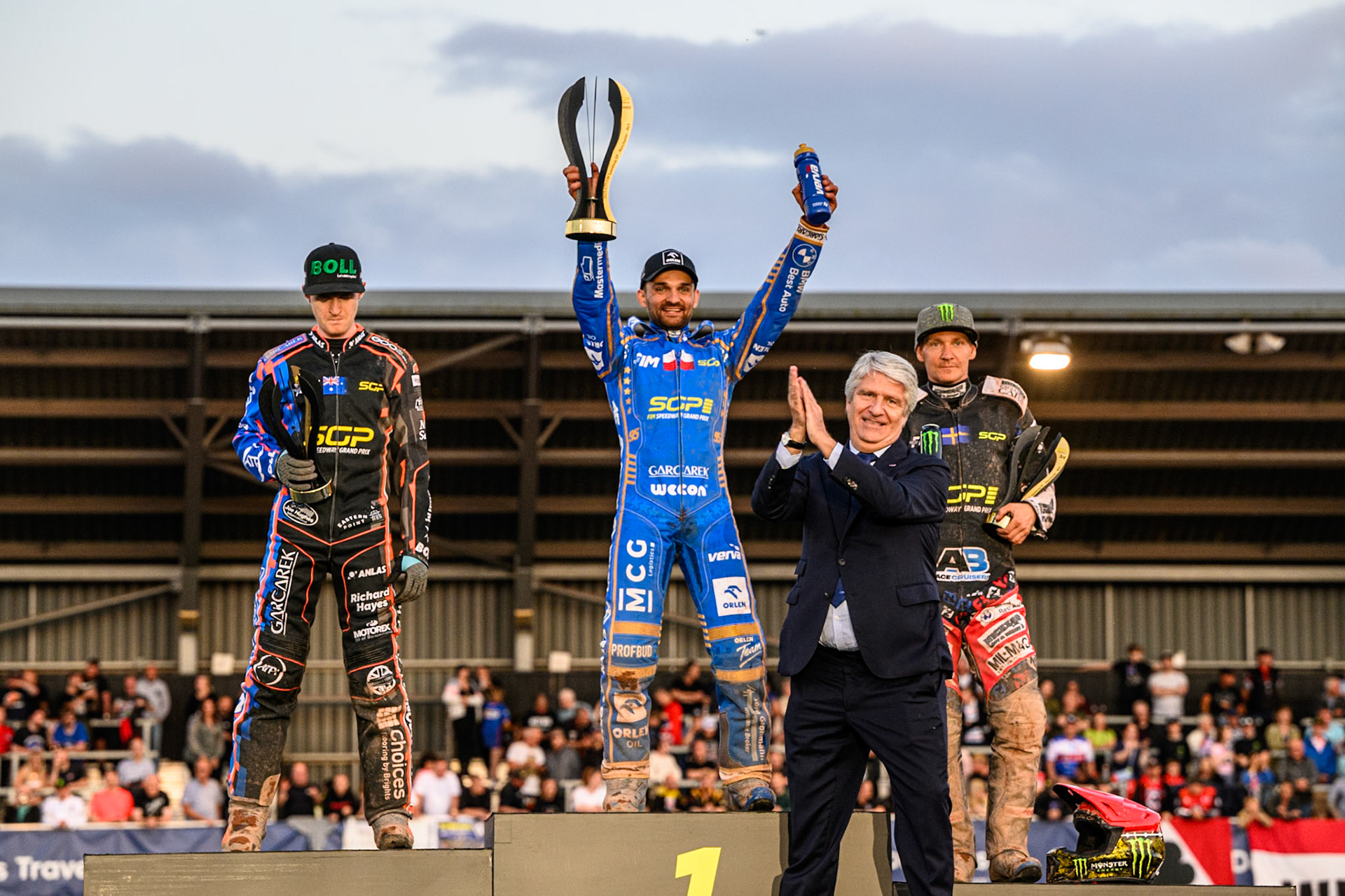 Top3: (L to R) Brady Kurtz (2nd), Bartosz Zmarzlik (First), Fredrik Lindgren (3rd) with FIM President Jorge Viegas (foreground) during the ATPI FIM Speedway Grand Prix Round 5 at the National Speedway Stadium, Manchester, on Saturday 14th June 2025. (Photo: Ian Charles | MI News)