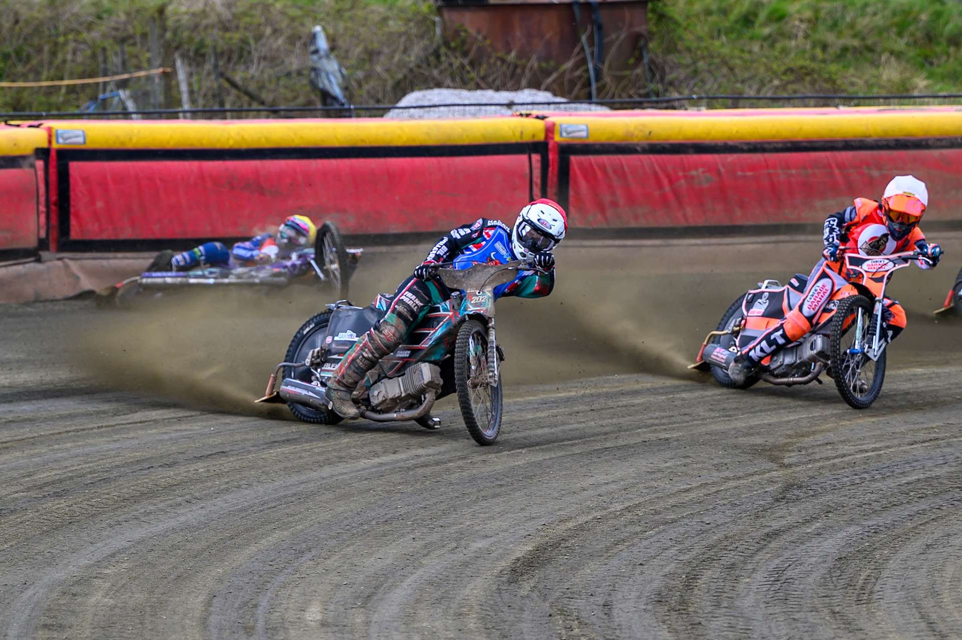 Alfie Bowtell of Buxton Bulls  in Red Connor Coles of NDL Nomads in White as Sam Woods of NDL Nomads  slides into the safety fence during the  Challenge match between Buxton Bulls and NDL Nomads at Hi-Edge Speedway, Buxton on Sunday 19th April 2026. (Photo: Ian Charles | MI News)