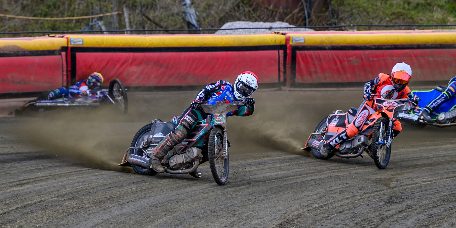 Alfie Bowtell of Buxton Bulls  in Red Connor Coles of NDL Nomads in White as Sam Woods of NDL Nomads  slides into the safety fence during the  Challenge match between Buxton Bulls and NDL Nomads at Hi-Edge Speedway, Buxton on Sunday 19th April 2026. (Photo: Ian Charles | MI News)