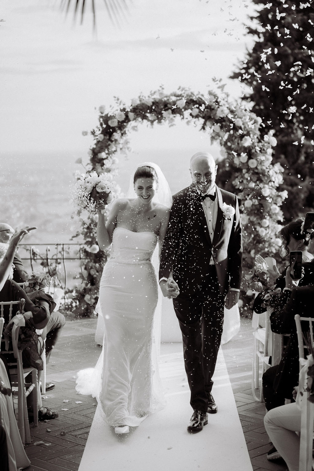 Fotografia di Arianna Macherelli, specializzata in Fotografia di Matrimonio, immagine in bianco e nero del lancio del riso mentre gli sposi camminano tra gli invitati