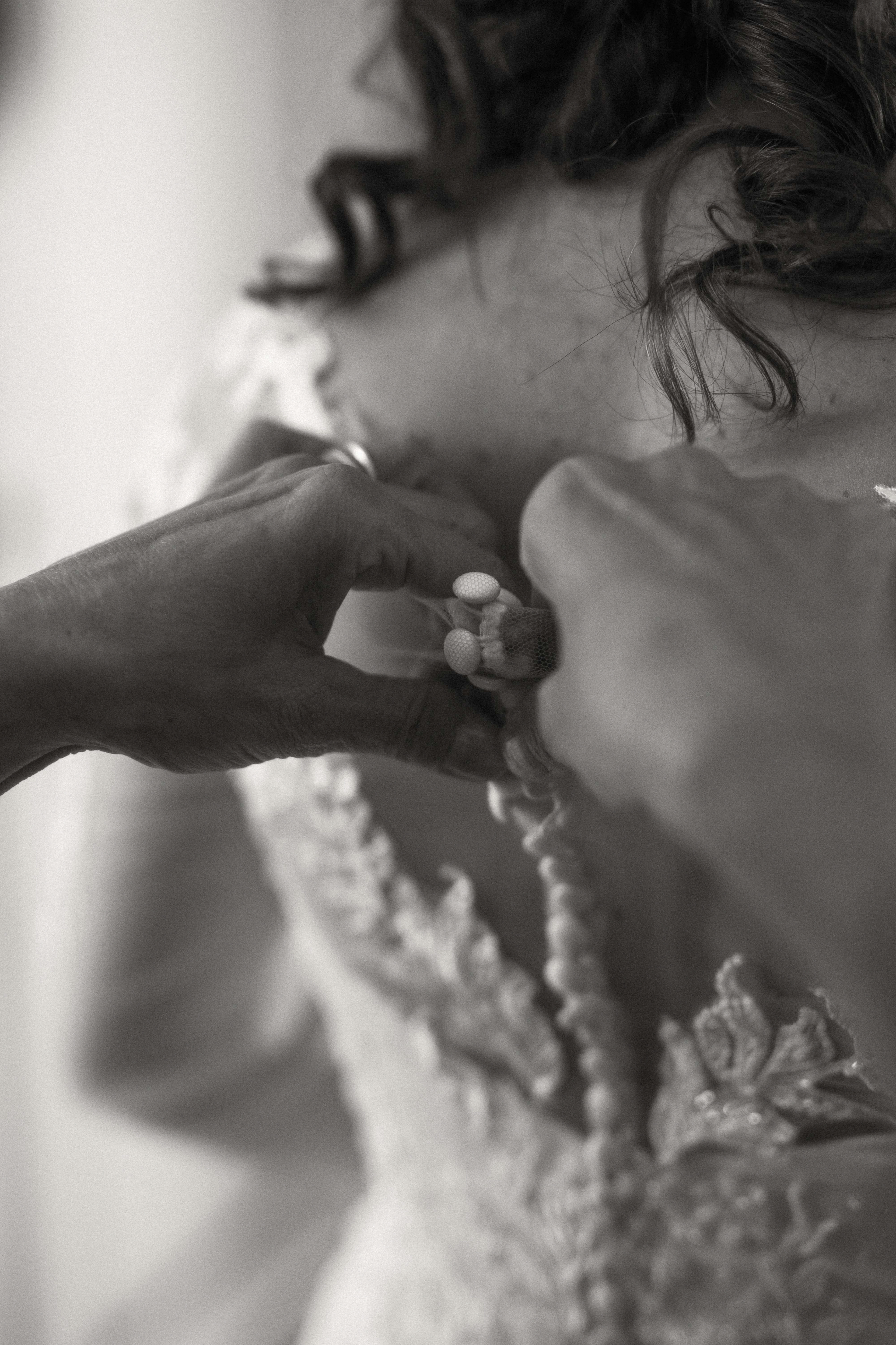 Fotografia di Arianna Macherelli, specializzata in Fotografia di Matrimonio, dettaglio delle mani che allacciano l'abito della sposa