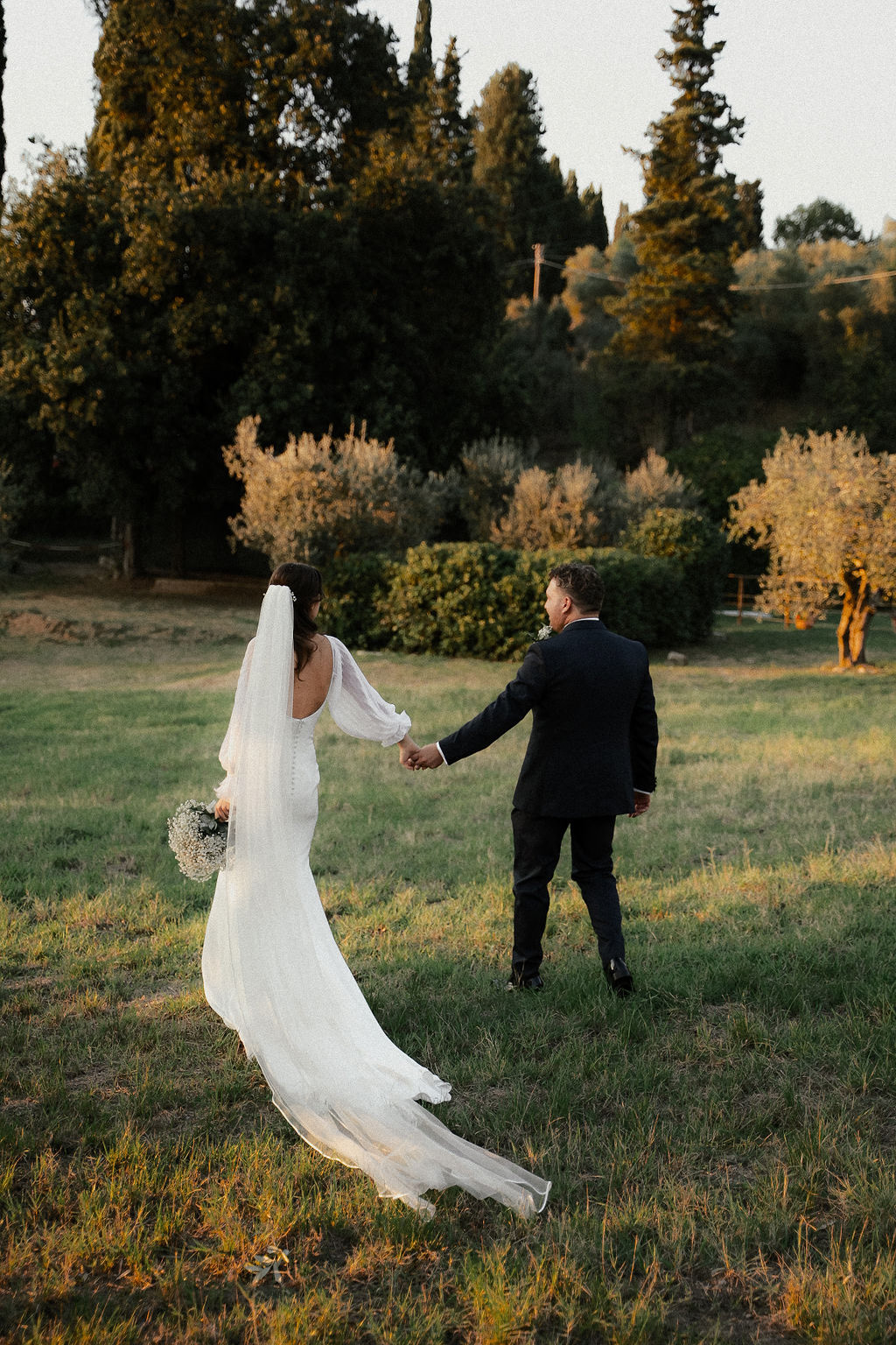 Fotografia di Arianna Macherelli, specializzata in Fotografia di Matrimonio, fotografia di spalle degli sposi mentre camminano mano nella mano immersi nella natura