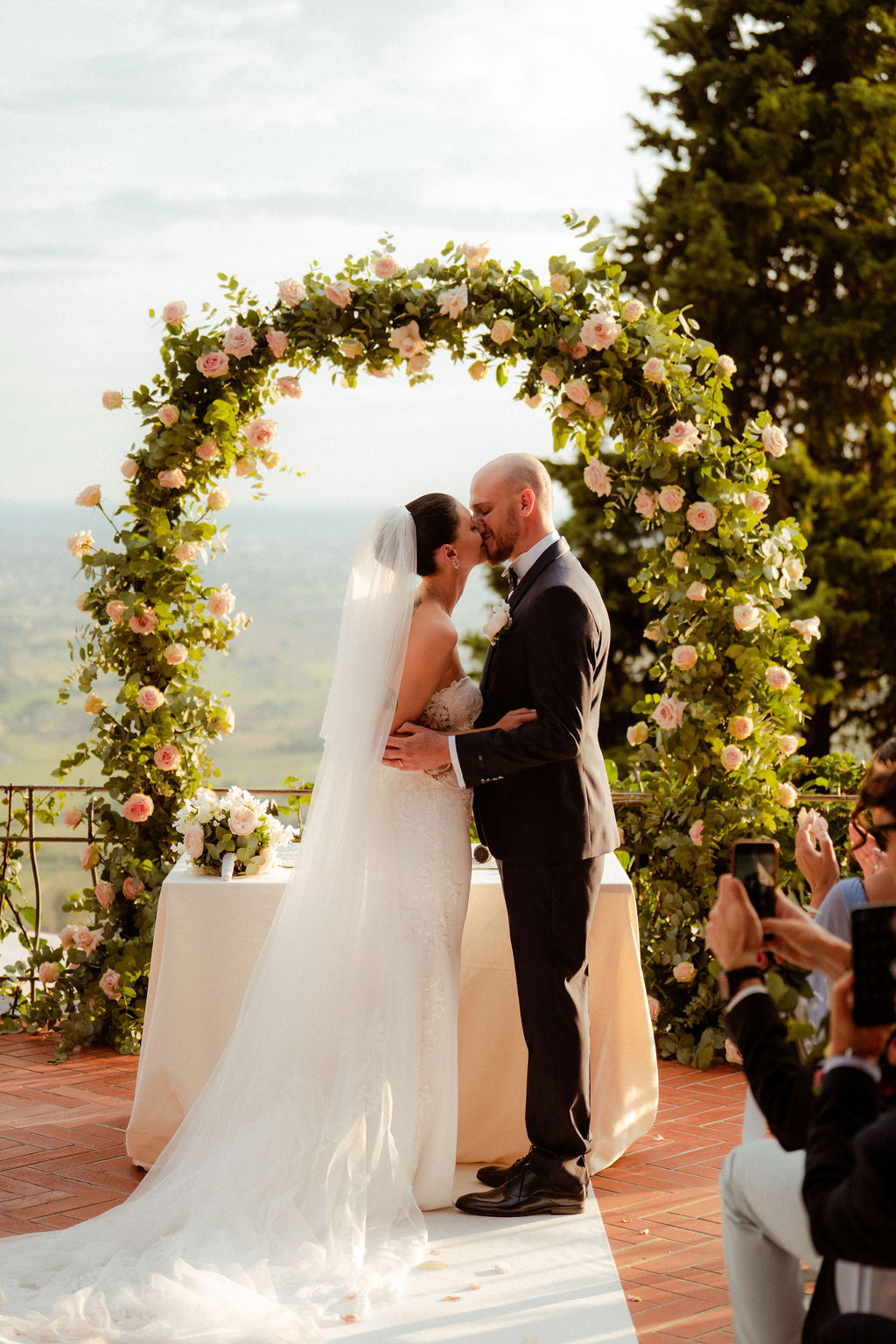 Fotografia di Arianna Macherelli, specializzata in Fotografia di Matrimonio, ritratto del bacio degli sposi con arco fiorito