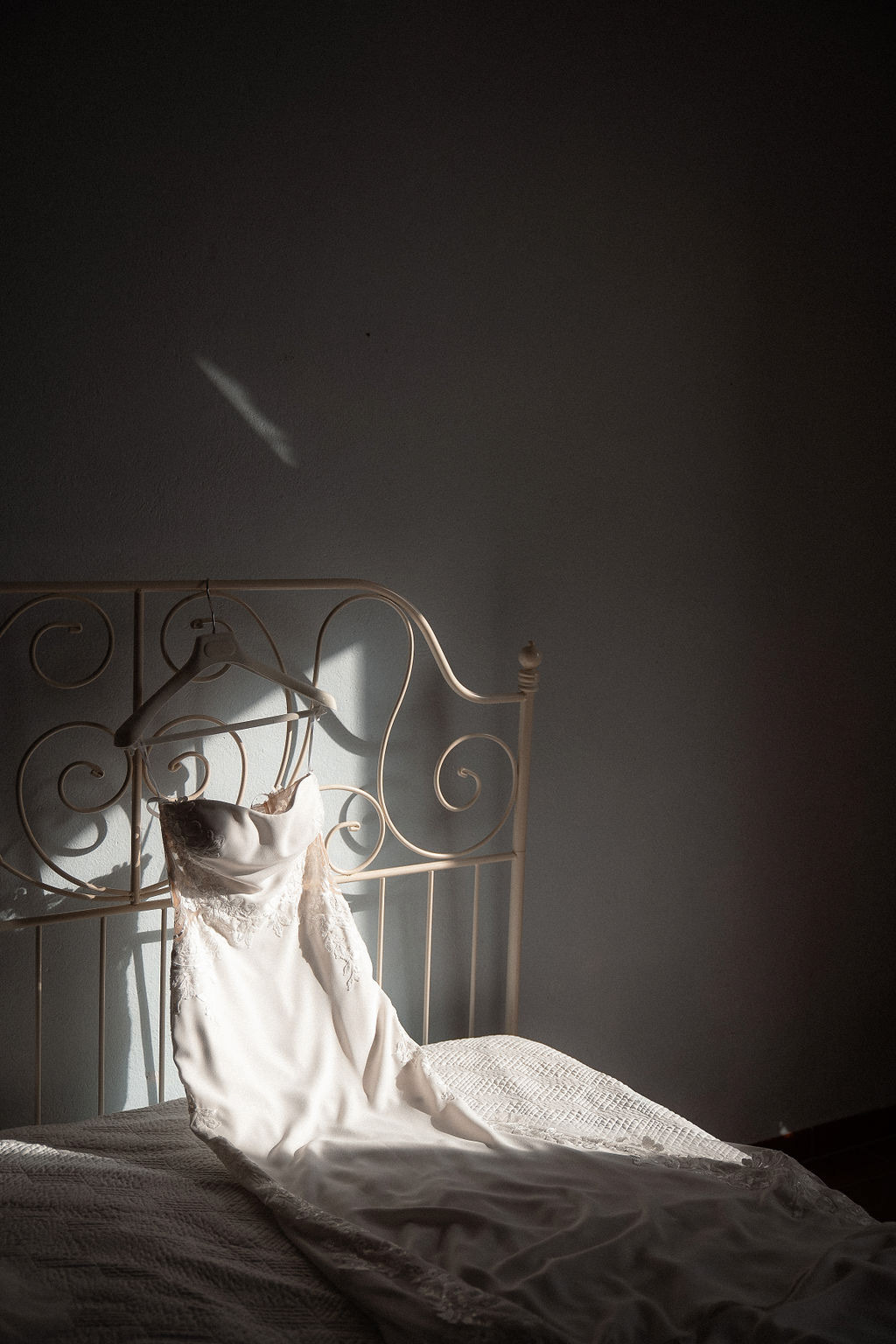 Fotografia di Arianna Macherelli, specializzata in Fotografia di Matrimonio, dettaglio di abito da sposa appoggiato sul letto con fascio di luce
