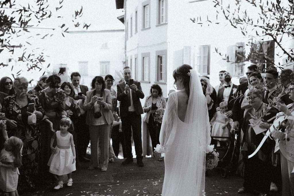 Fotografia di Arianna Macherelli, specializzata in Fotografia di Matrimonio, immagine di reportage della sposa che ammira gli invitati dopo il lancio del riso