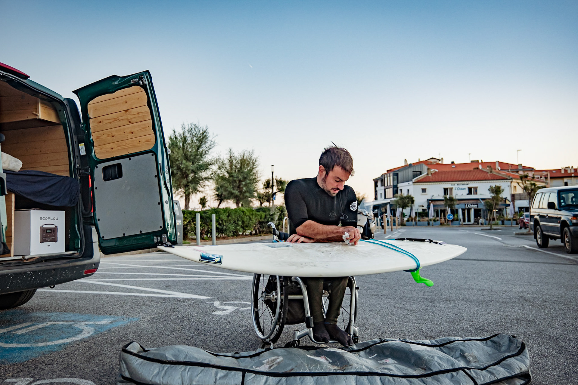 Maixi Cabanne membre de l'équipe de France de para surf avant une session en complète autonomie. Il waxe sa planche avant d'aller surfer.Sous légendeFrance, Hossegor, 2022-09-22. Camp de selection de l'equipe de France de para surf pour les championnats du monde. Le surf lui a appris a etre patient. « Je vais tous les jours à l’eau, c’est un exutoire, on se sent lave apres une session. L esprit va mieux. Je sors d’un ete de 2 mois d’arret de surf, a la suite d’un pneumothorax. Le surf est une passion, je ne pourrai pas m’en passer. » Maixi avant une session en complete autonomie. Il waxe sa planche avant d'aller surfer. La wax est une cire utilise par les surfeurs pour ne pas glisser sur leurs planches. Photographie de Romain de Sigalas / Hans Lucas.