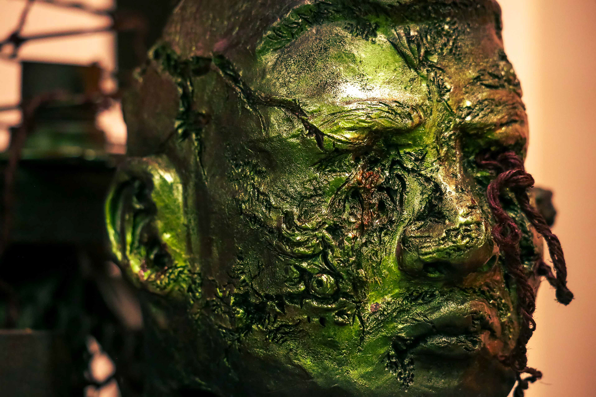 Close up of "A Sacrifice" sculpture, showing a decaying, heavily textured green head. Piece by Mtende Moyo.