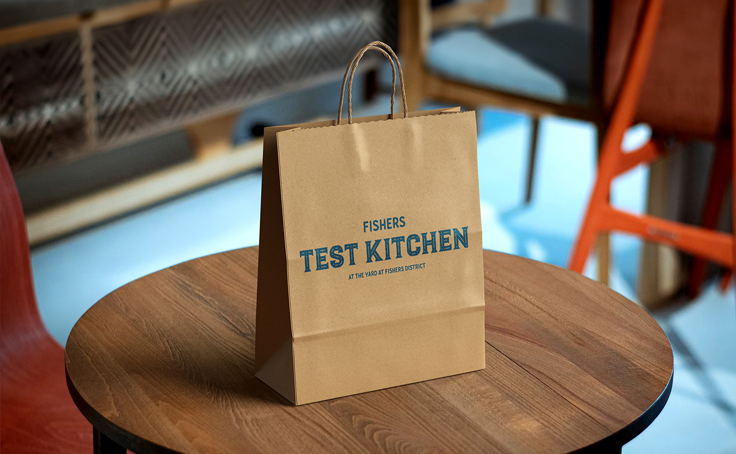 A to-go bag with the logo of the Fishers Test Kitchen printed on the front sitting on a table