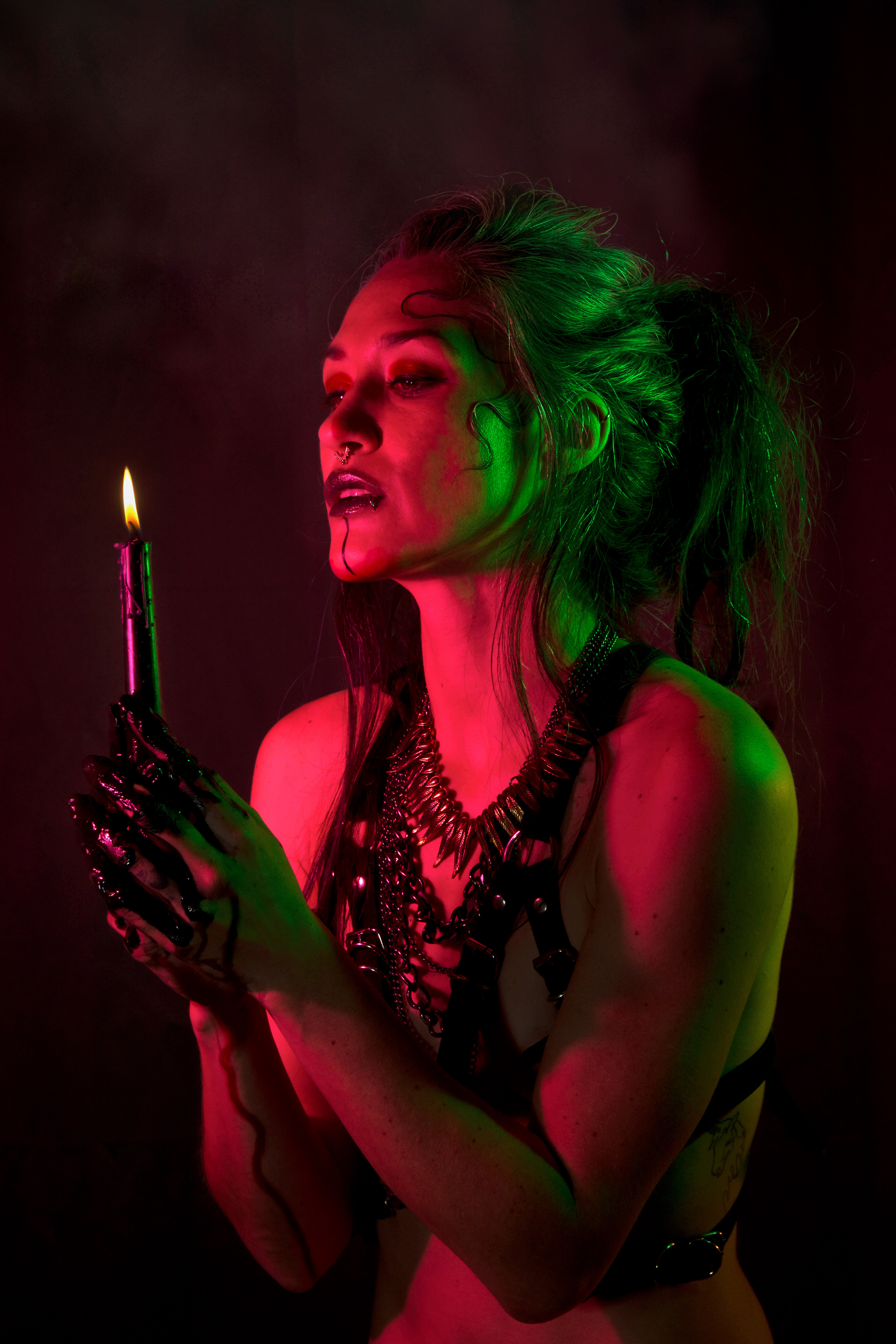 Studio artwork, portrait, colors red and green, woman holds black candel. Accessories MUA