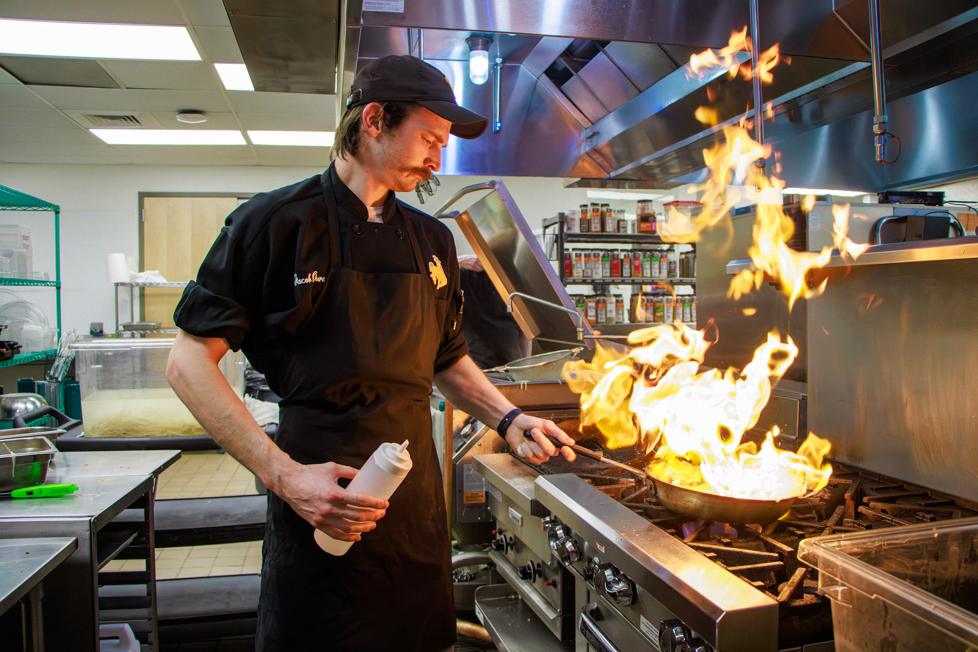 Jacob Ourada flambeés asparagus at the University of Wyoming High Altitude Performance Center in Laramie, WY, Thursday, March 9, 2023. As the Performance Chef for the university's athletes, Ourada adds extra char to the stalks during a make-your-own pad Thai bowl dinner.