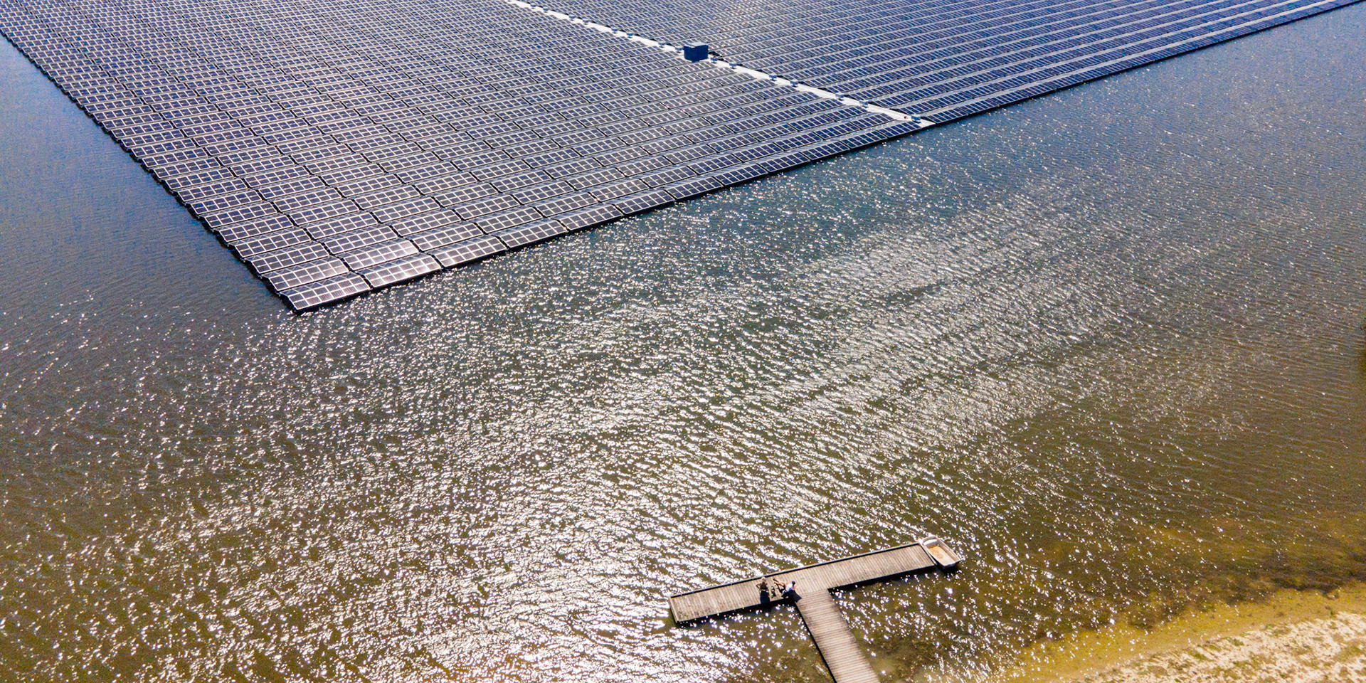 People on jetty enjoying beautiful landscape with floating solar panels in water in wide landscape.