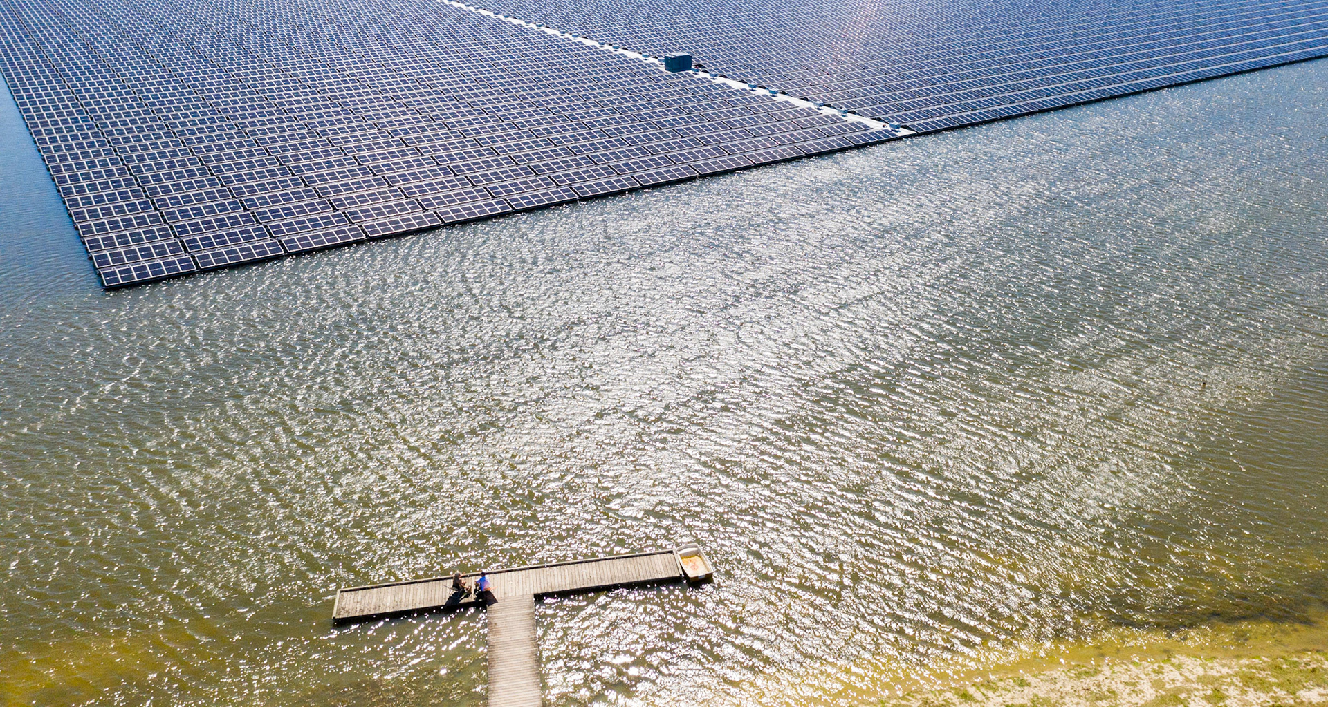 People on jetty enjoying beautiful landscape with floating solar panels in water in wide landscape.