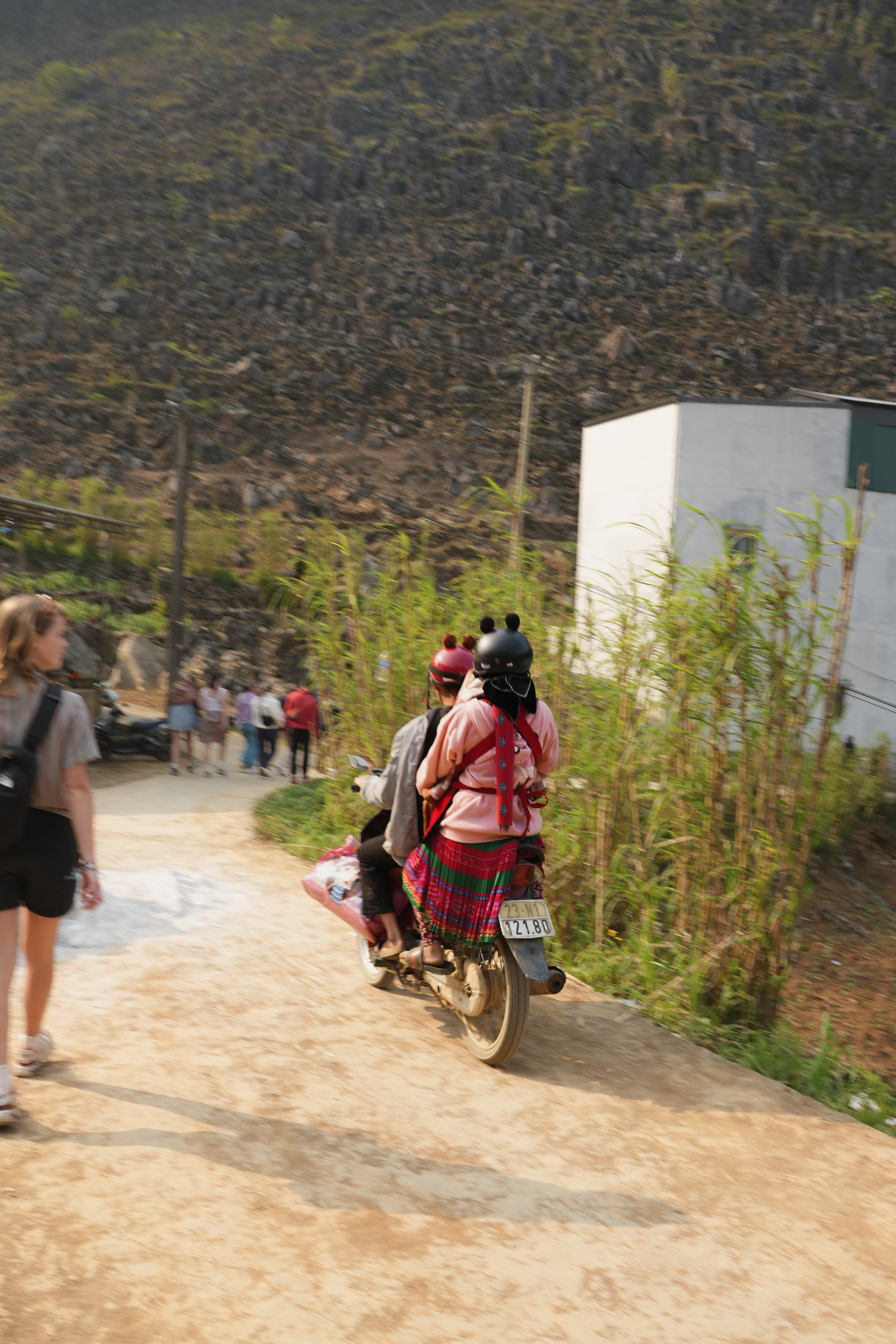 A couple rides their motorbike through Ha Giang province, carefully making a path for themselves as tourists move in the same direction. Where are they going? Are they on their way to work, or enjoying a quiet date? How long have they been together, or are they even a couple? Will people step aside to let them pass? Is the nearest village waiting at the end of the path? How old is the bike? Are they married? And most of all, what are their names?