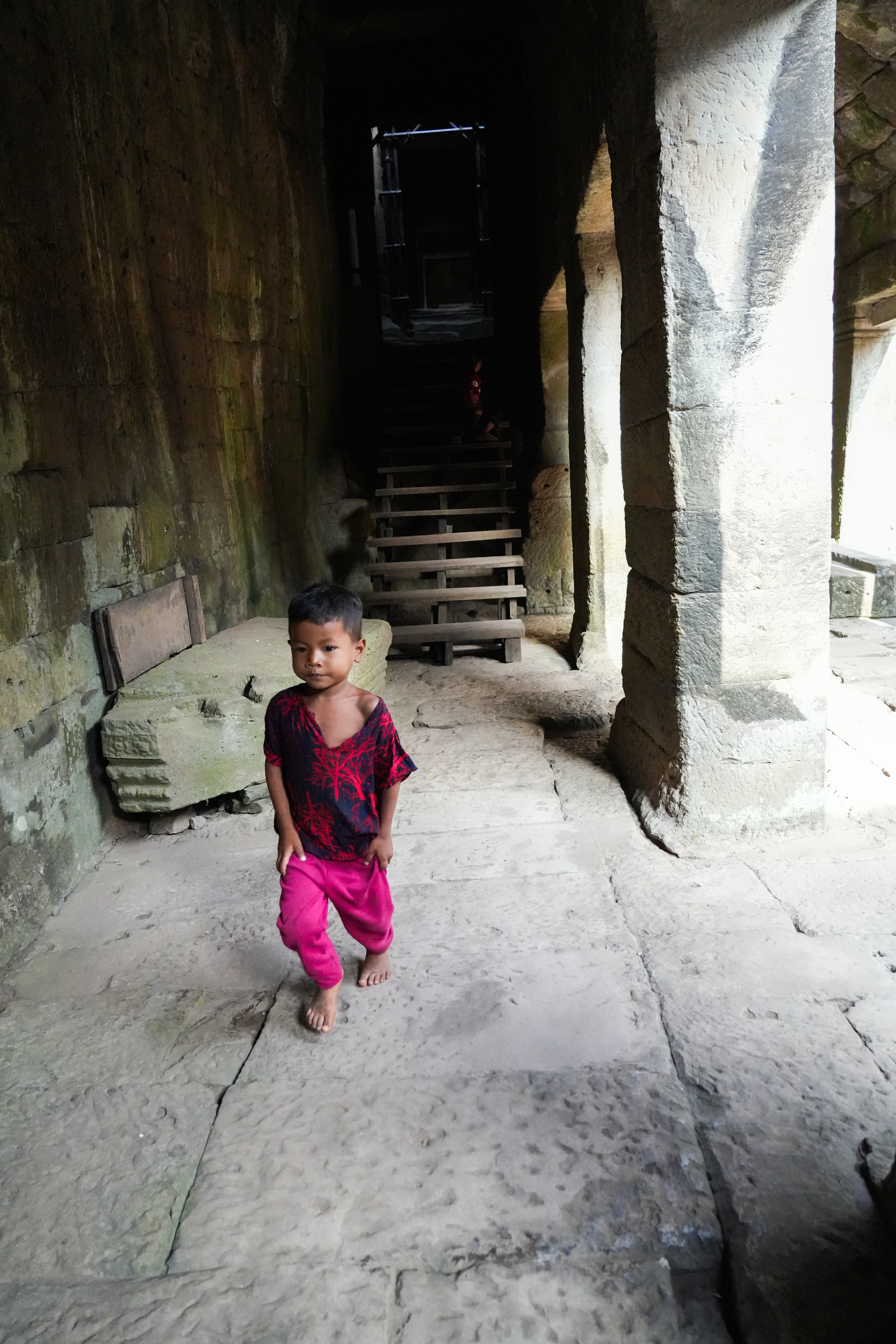 Continuing my visit, like many tourists that day, like every day. I came across a Little Boy, almost a baby, moving alone through the Bayon Temple, this multi-faceted 12th-century monument. Around him, tourists shuffled in and out of doorways, cameras clicking, voices echoing against what remains of the walls. His colourful silhouette contrasted the monotony of the surroundings. He moved slowly, not rushing, as if the crowd didn’t bother him. I kept wondering if someone was watching over him. I imagined who might be waiting for him, where he belonged? Is he safe, alone, at such a young age? Has he walked these paths before?Is someone waiting for him at the end of this corridor? Has he been told stories about this place or is it just a playground to him? Does he understand the history written in these stones? If I spoke to him, would he speak back? Would he tell me his name? Then… What is his name?