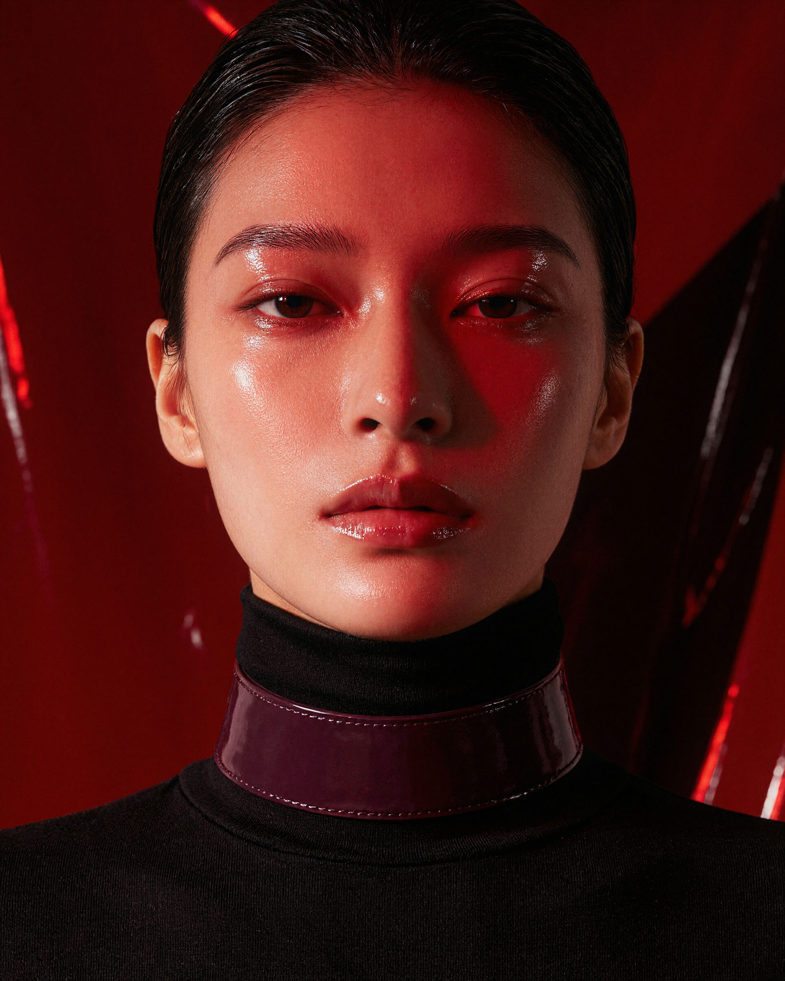 Portrait of a woman in a black turtleneck and glossy burgundy collar, lit in deep red