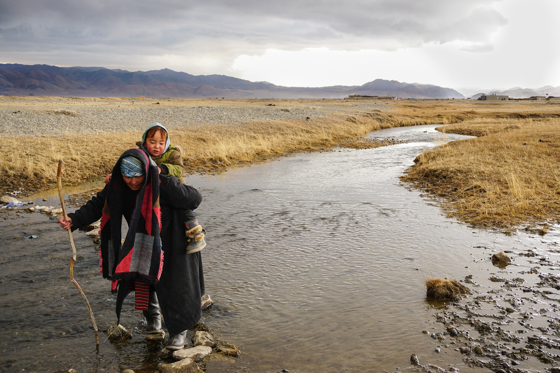 A woman helps her grandson cross the river, Mongolia.