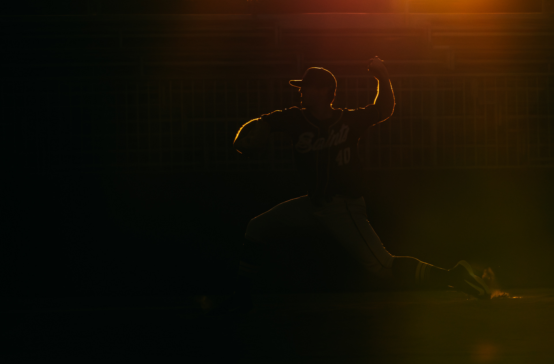 College baseball pitcher throwing a pitch in shadows during a California Collegiate League baseball game at MLB Academy in Compton, CA