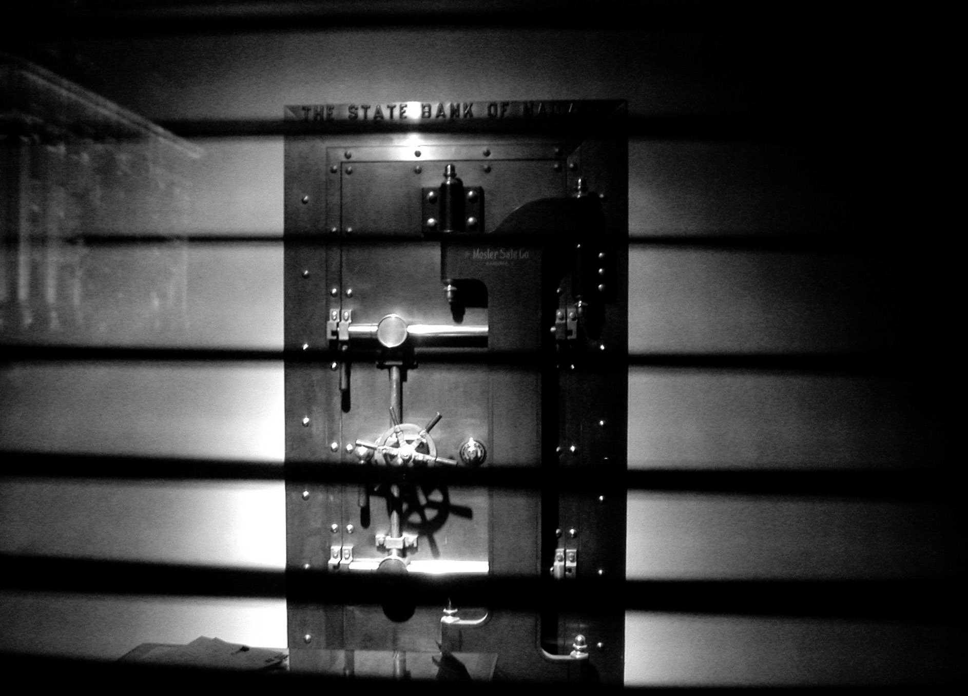 Bank vault door viewed through window at night.