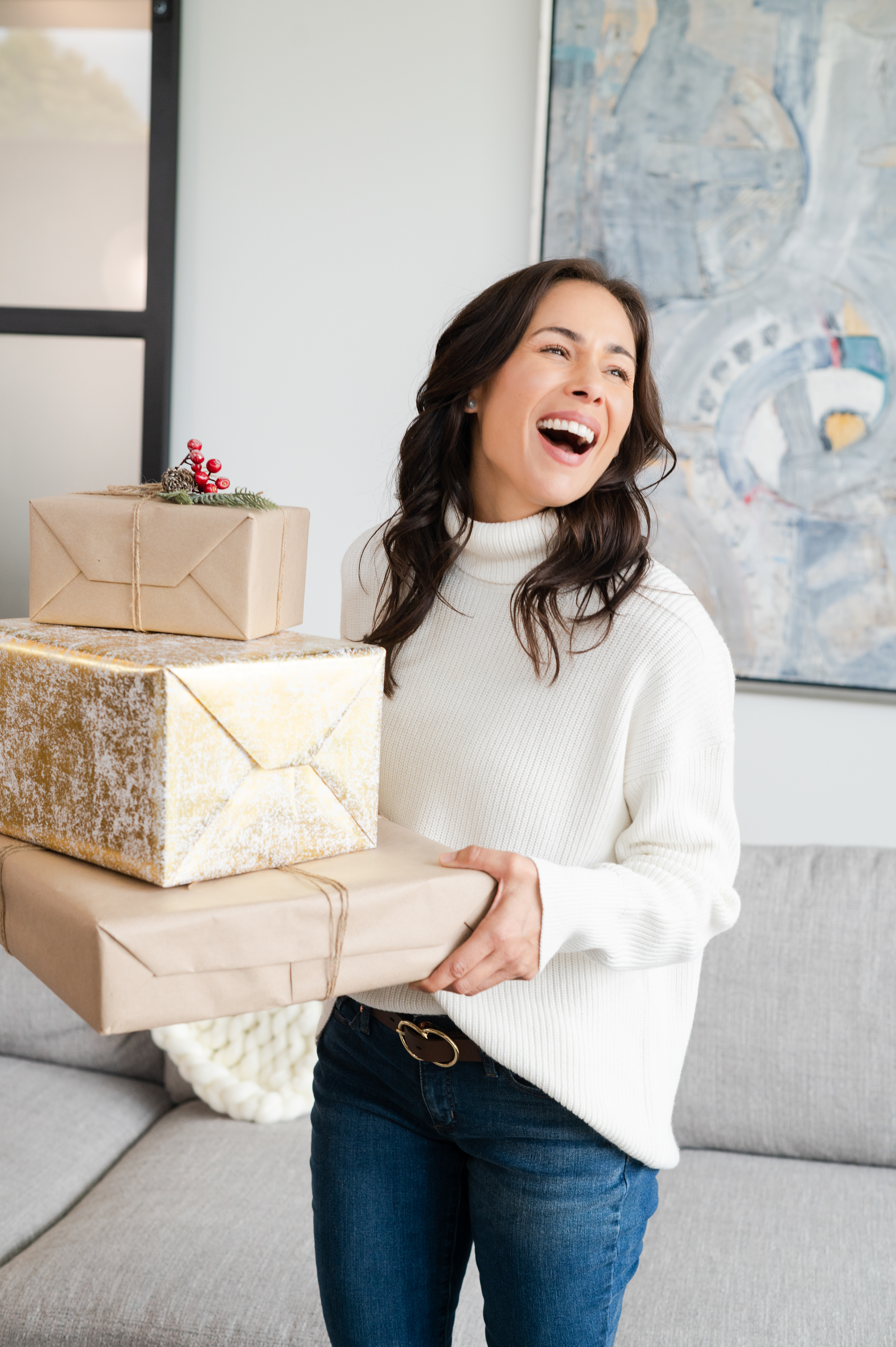 Brunette model standing in a living room holding a stack of wrapped packages