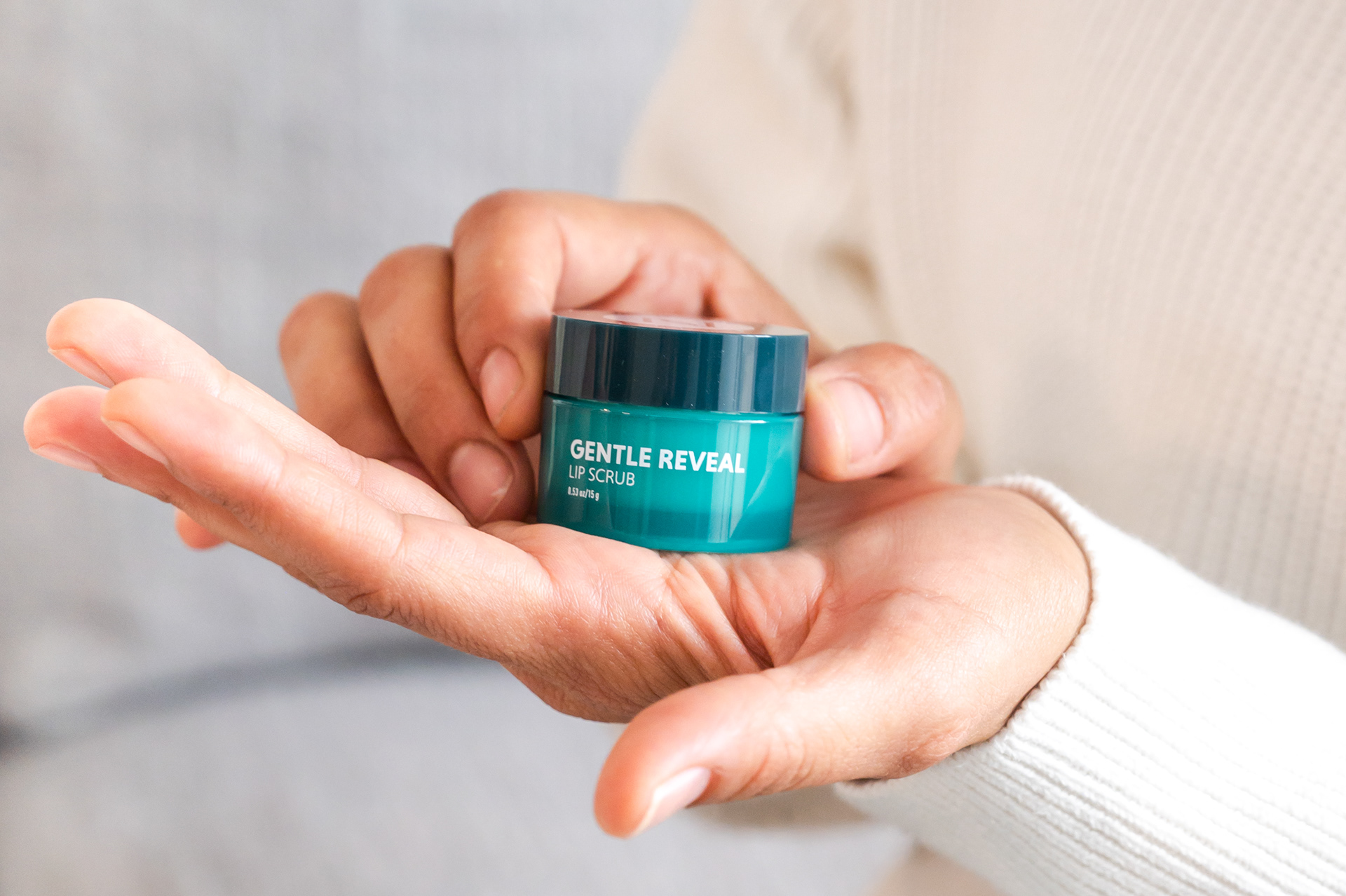 Close up of hands holding a tub of Neora Gentle Reveal Lip Scrub