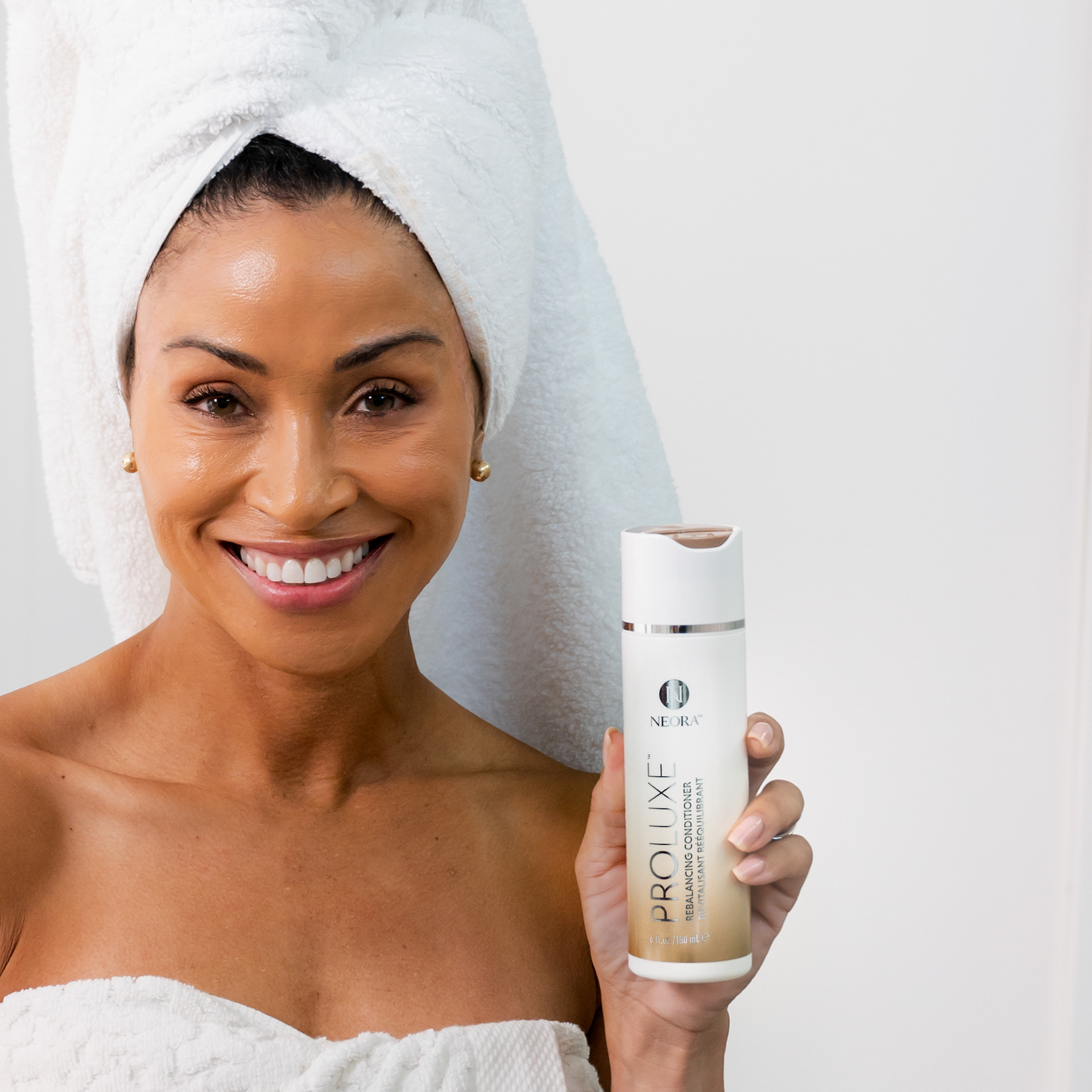 Model with hair wrapped in a towel holding Neora shampoo bottle.