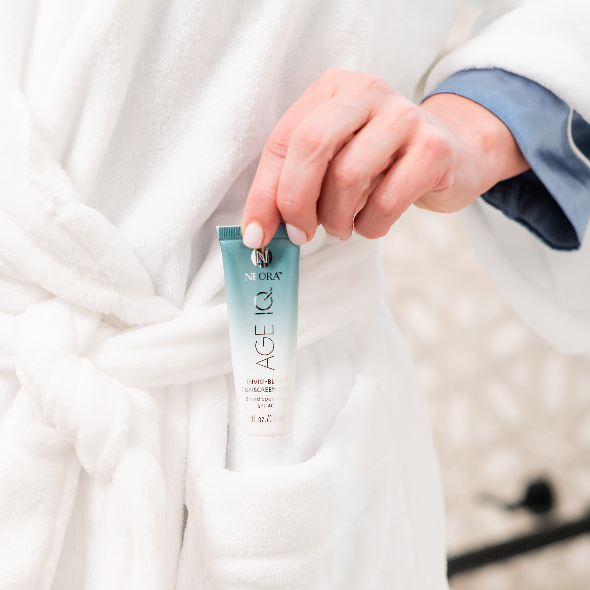 Woman pulling Neora Age IQ tube out of the pocket of her white bathrobe