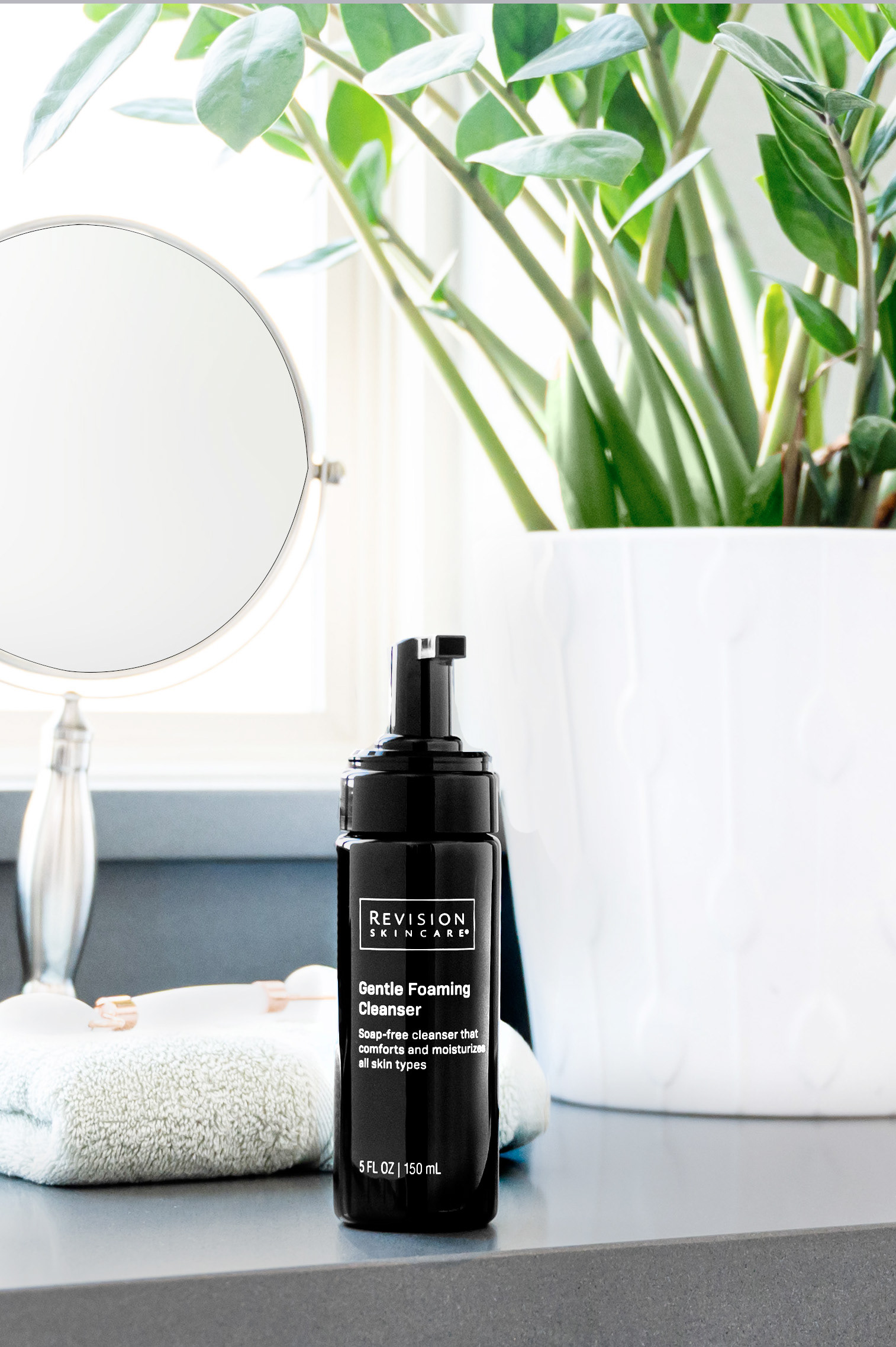 Revision Skincare Gentle Foaming Facewash styled on a bathroom counter with a mirror and plant in the background