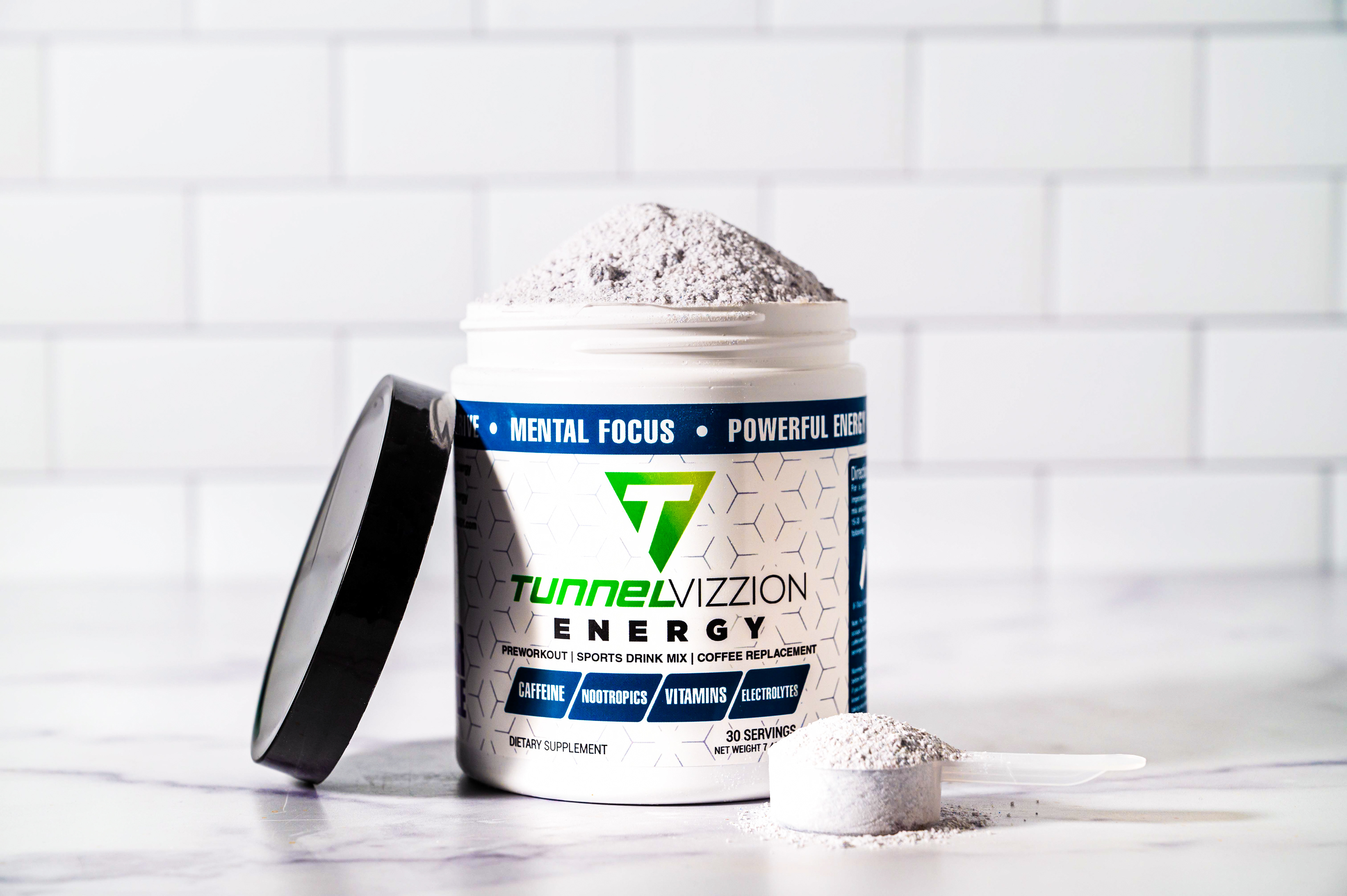 Powder heaping over the top of an open can of Tunnel Vizzion Energy powder against a white subway tile background