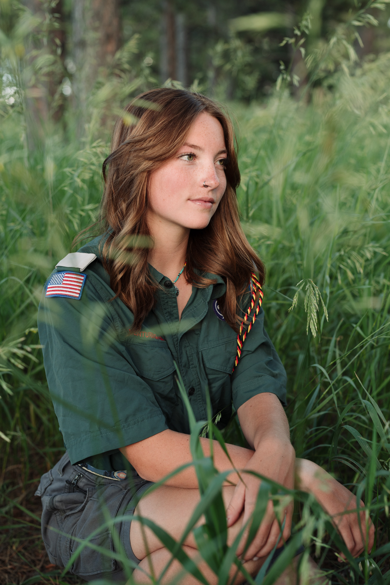 Senior portrait of a girl in a scouts uniform in grasses and looking off in the distance.