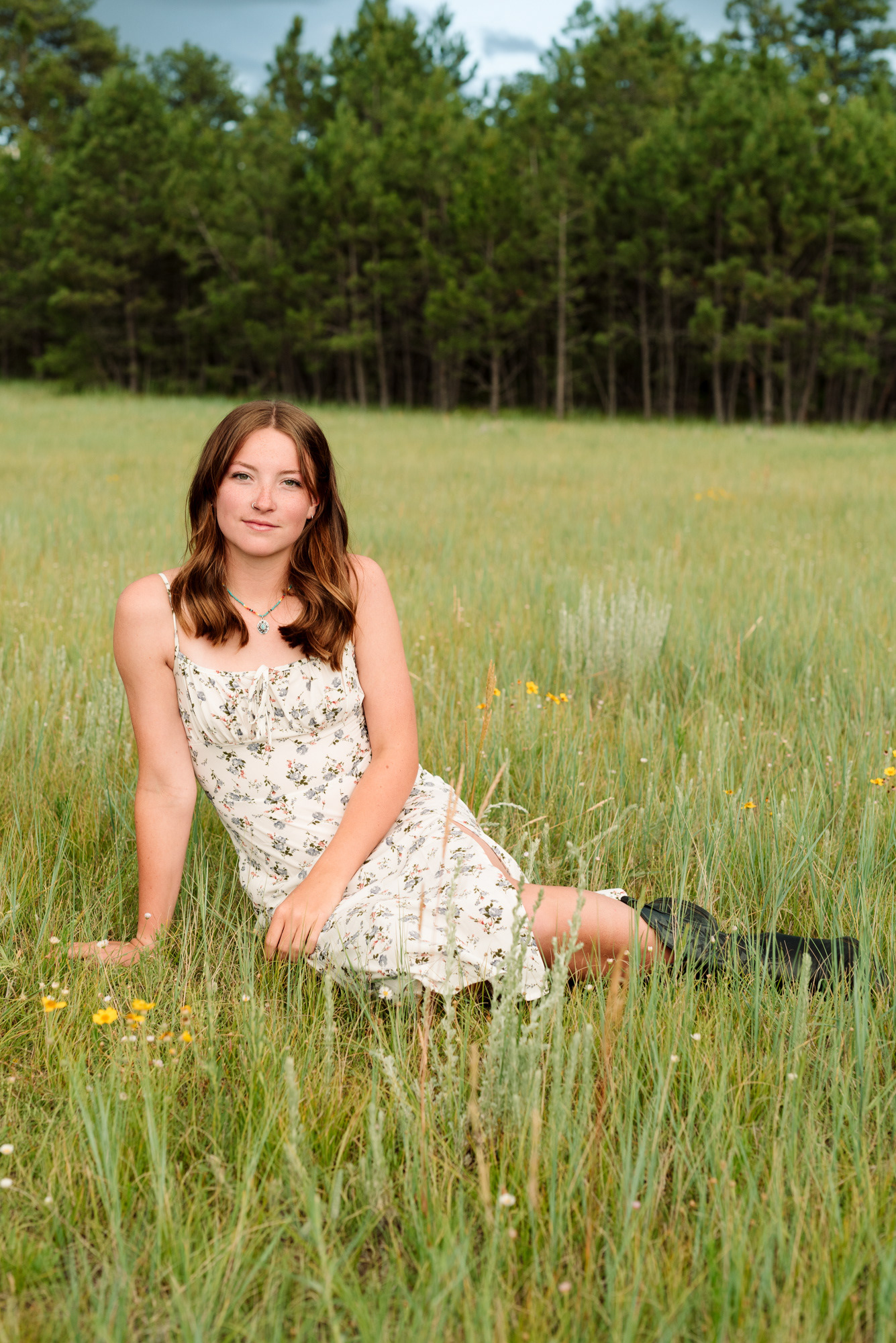 Portrait of a high school senior wearing a summer dress and sitting in long grass in Colorado.