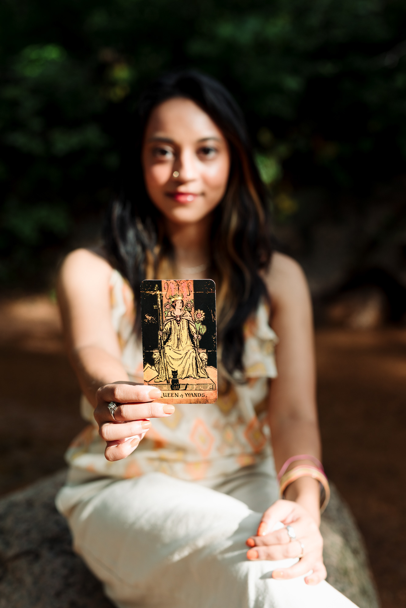 Woman holding up a Queen of Wands tarot card with her face blurred in the background.