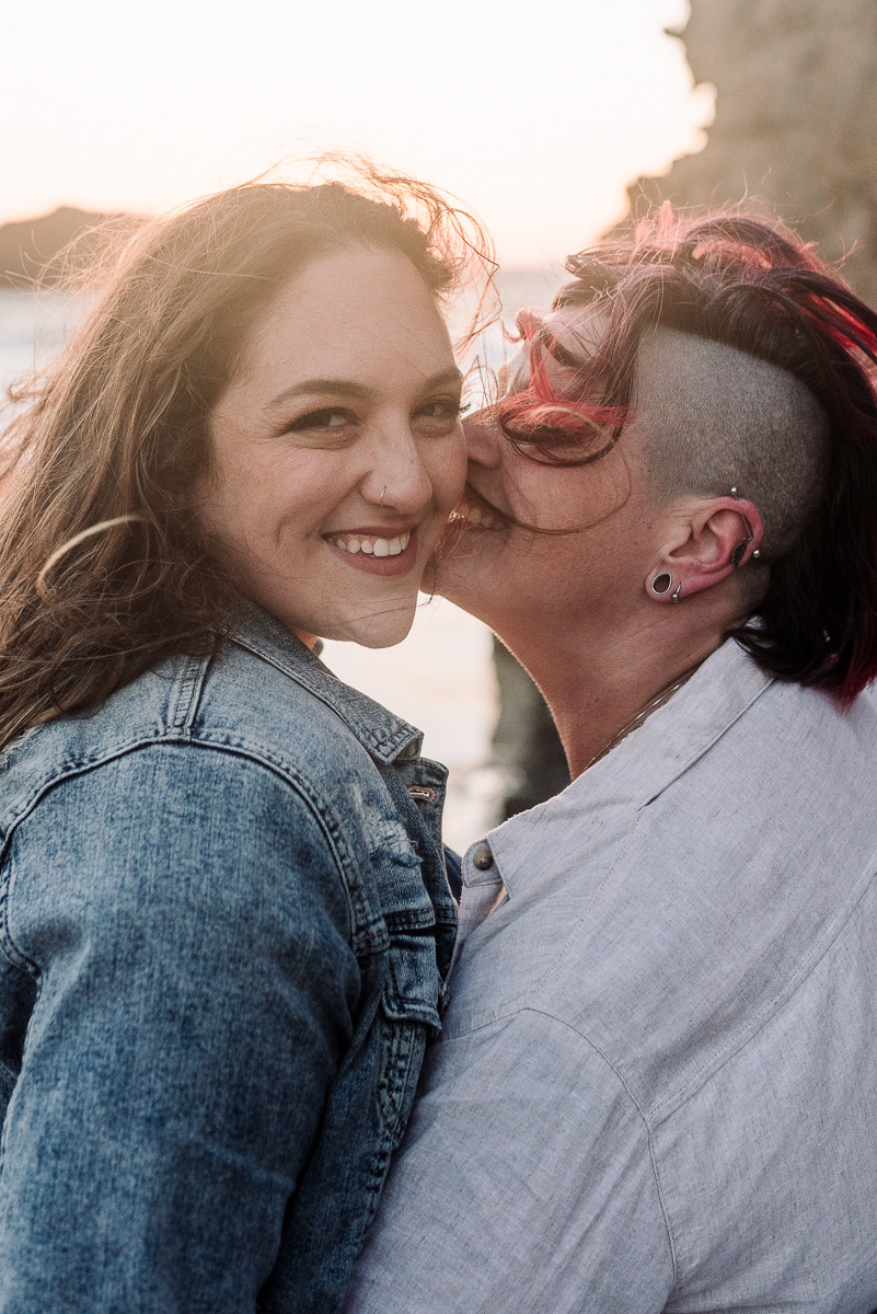 Portrait of a woman with pink hair kissing the cheek of another woman.