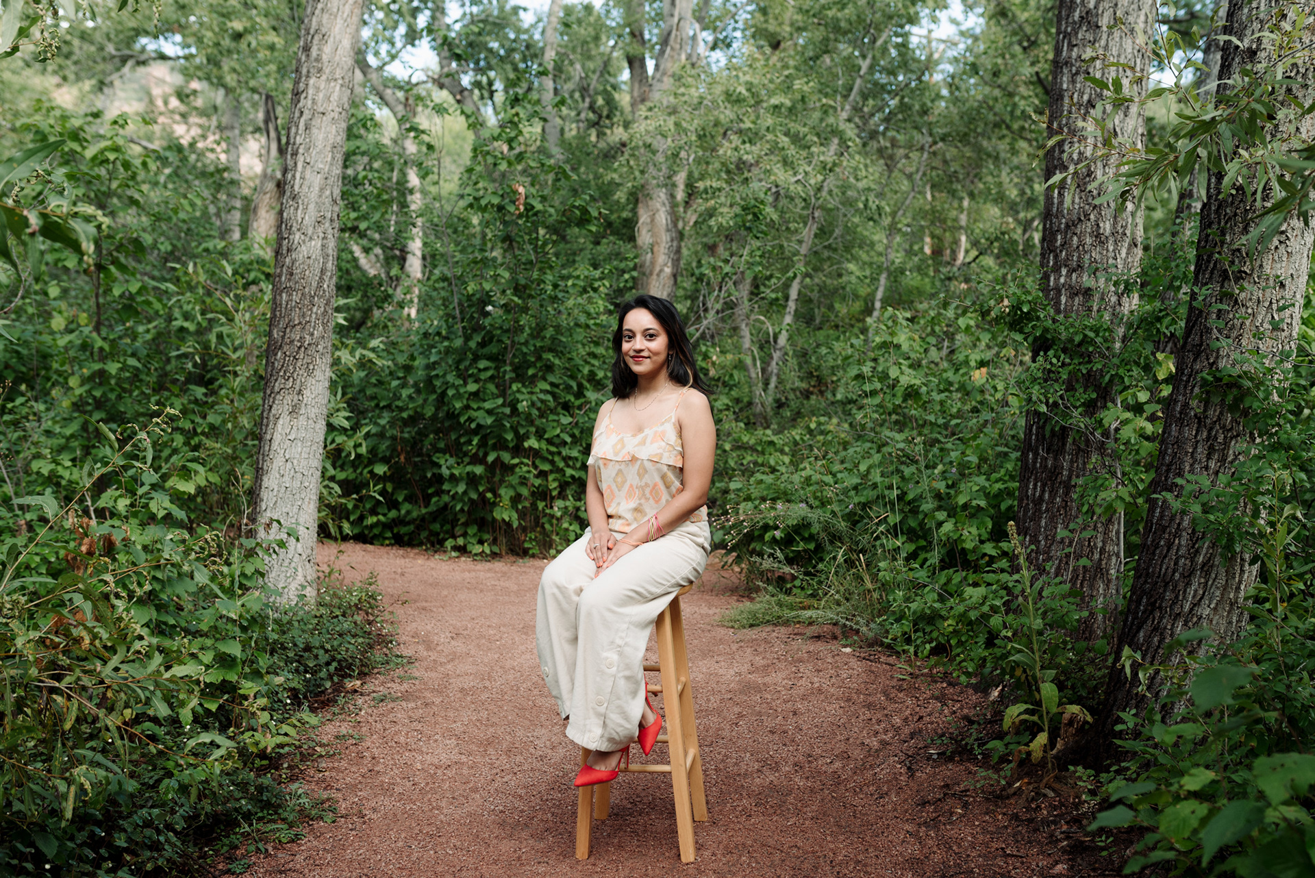 Portrait of a woman sitting on a wooden stool in a forest.