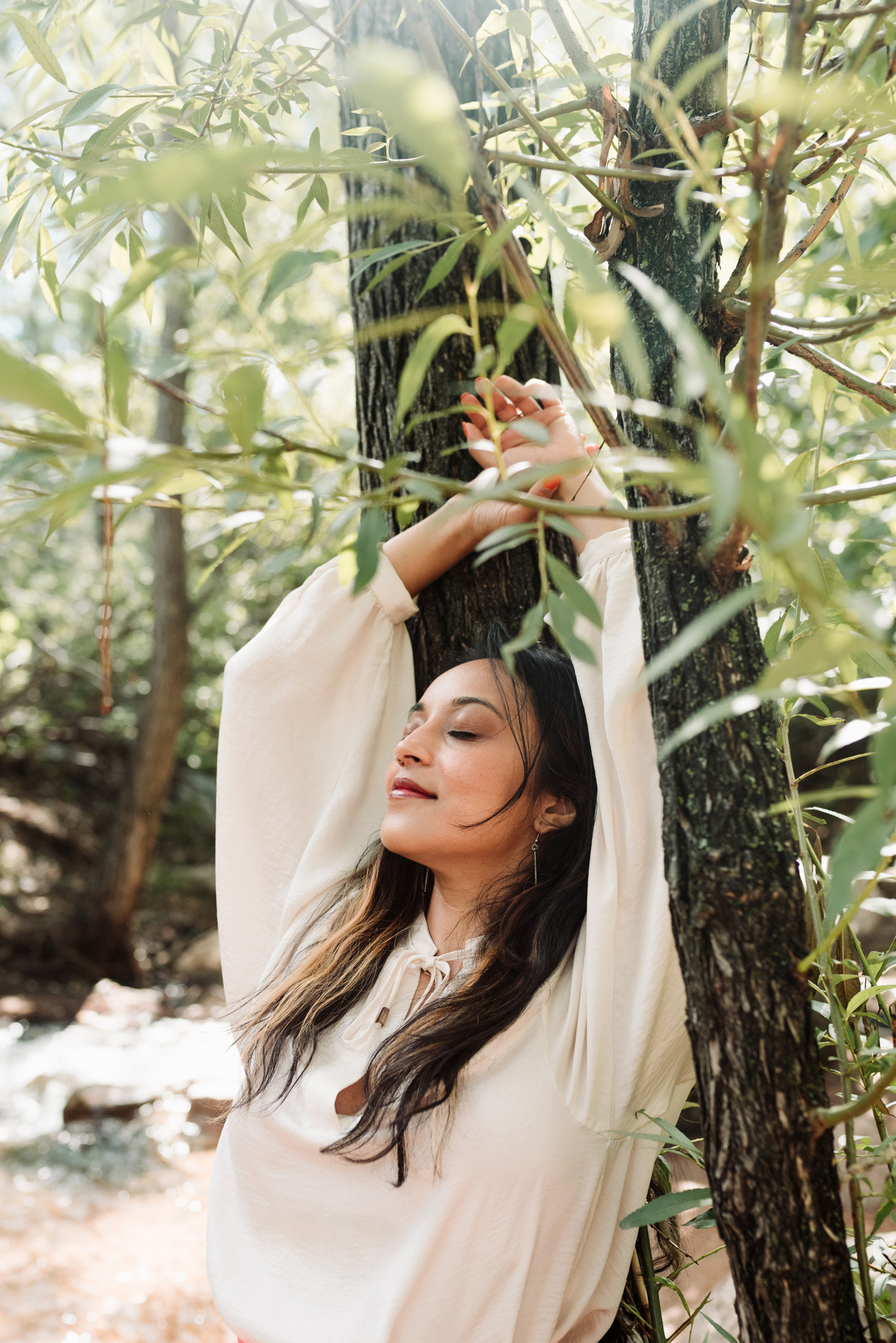 Woman relaxing against a tree beside a river.