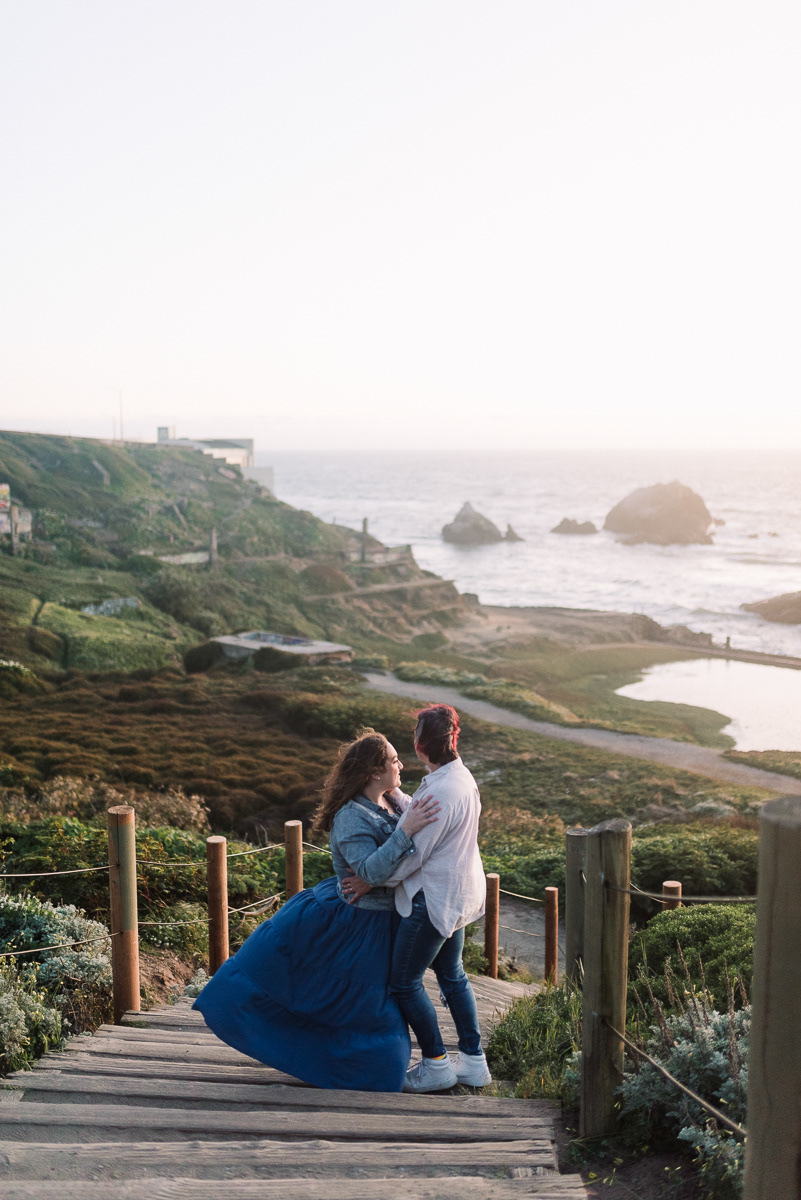 Two women embracing at the top of stairs overlooking the ocean.