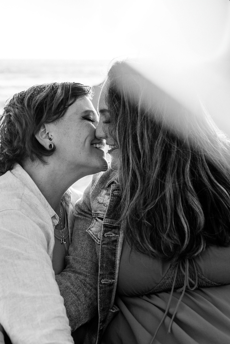 Black and white portrait of two women leaning in to kiss with a sunflare.