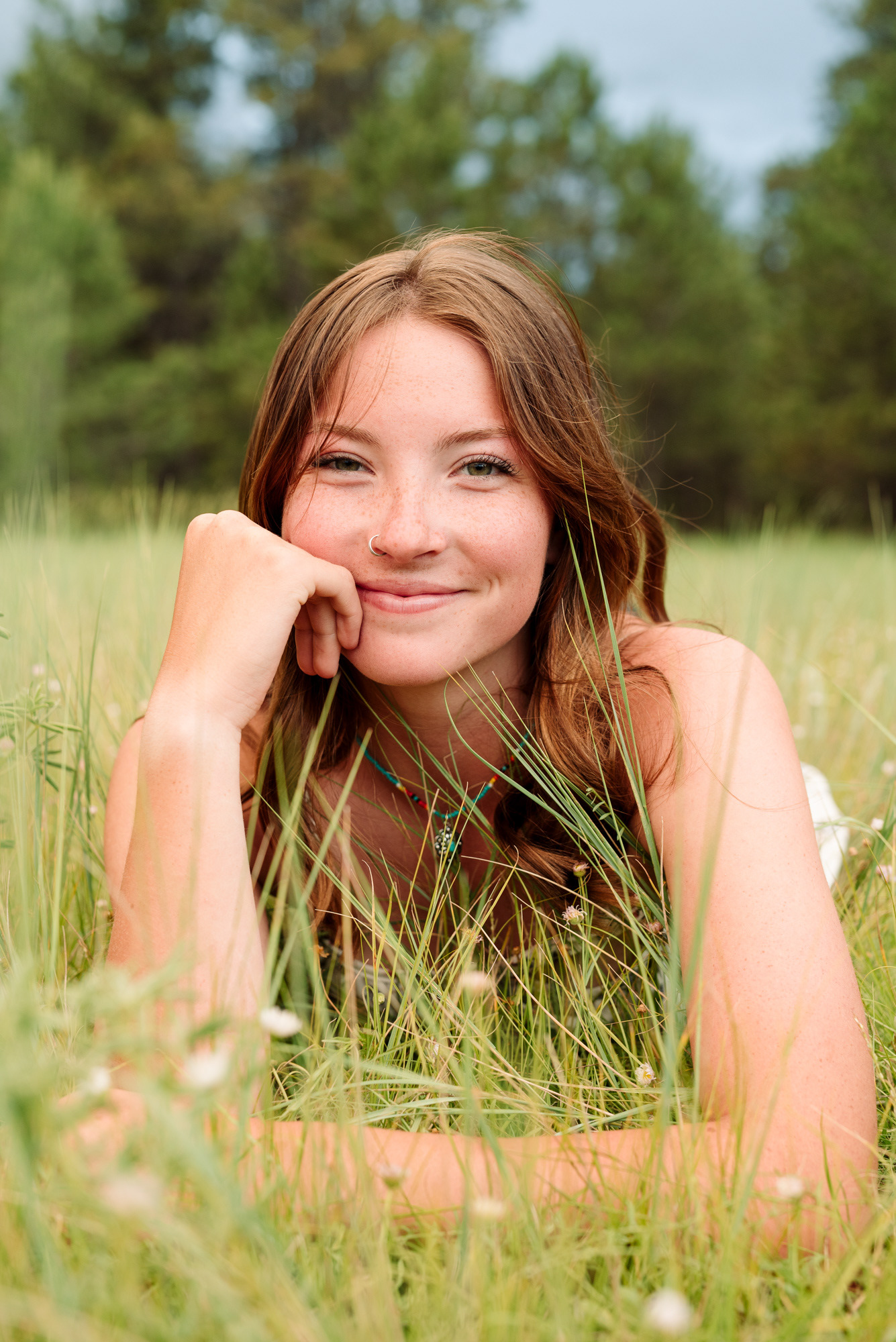 Smiling portrait of a high school senior lying down in grasses and flowers.