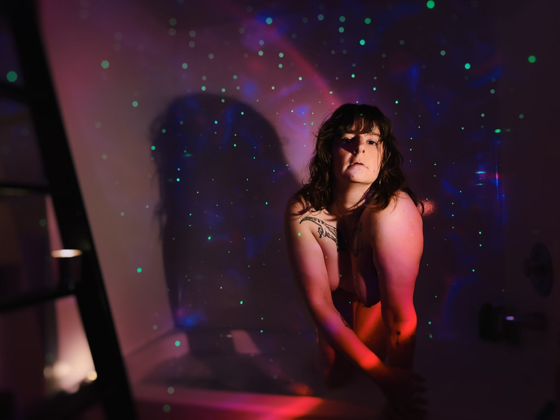 Image description: Sami was in the bathtub naked. She looked at the camera. There was a galaxy projector on the wall.