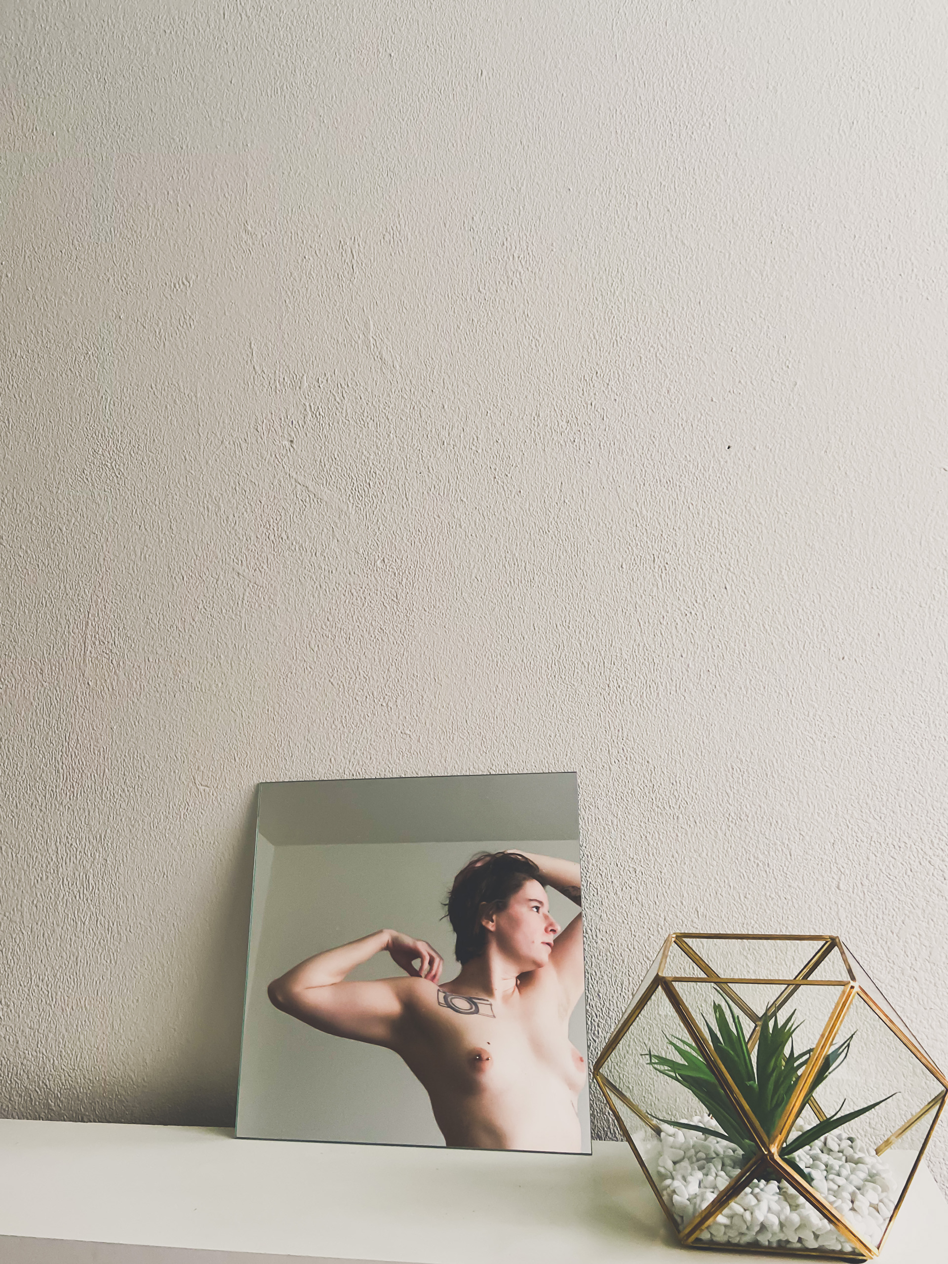 Image description: Sami was posed naked through the mirror on the counter. 