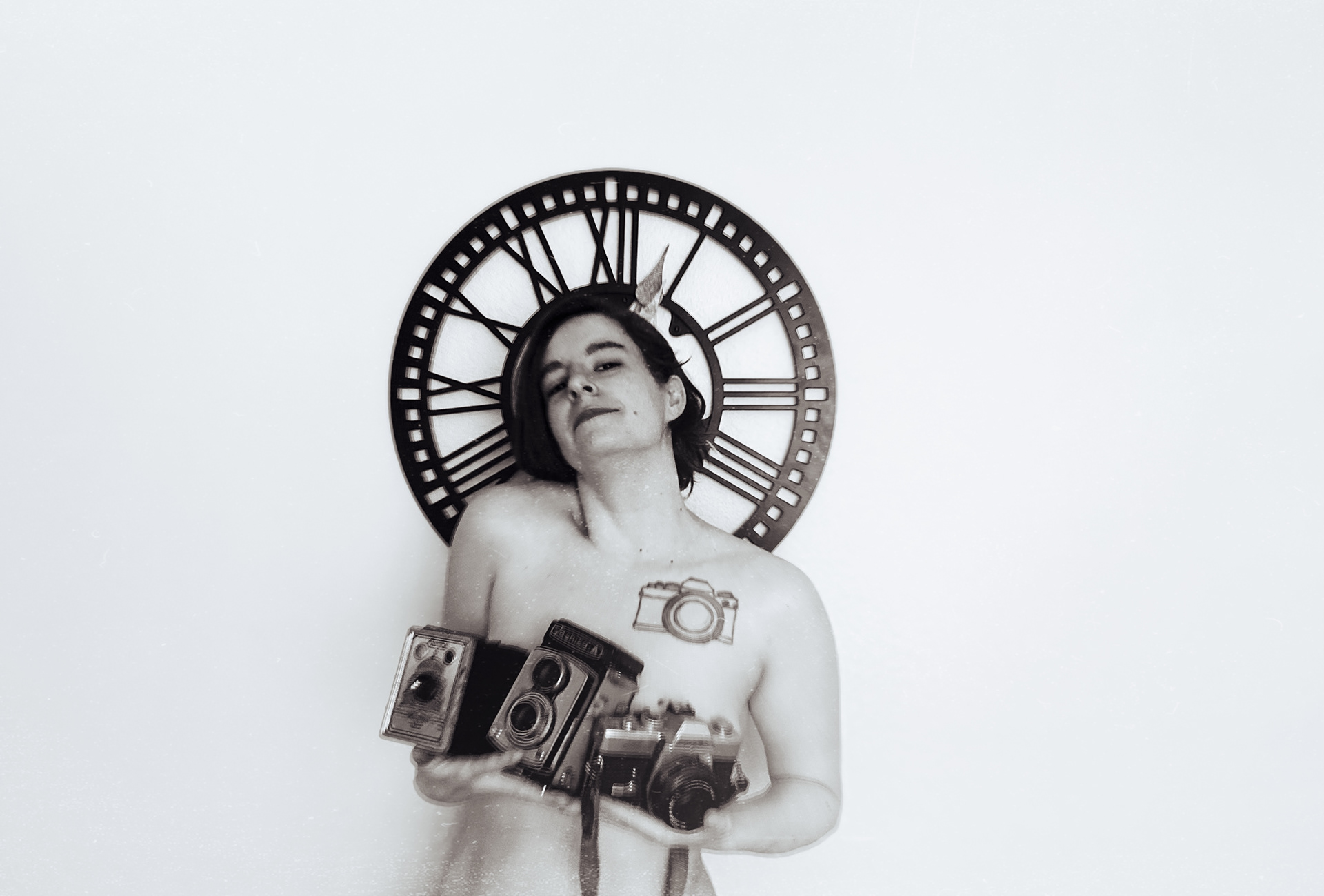 Image description: Sami was topless holding her collection of film cameras. She was smiling at the camera. There was an old fashion clock behind her. The picture was in the black and white.