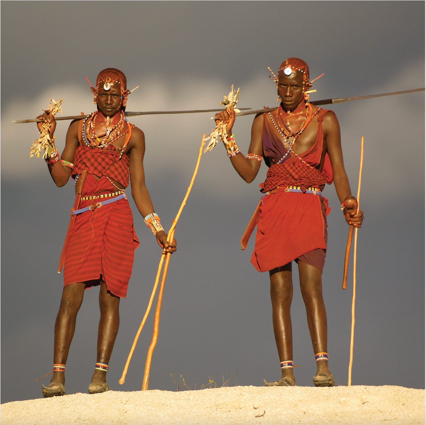 Two Maasai warriors in traditional red shuka and beadwork, holding spears, Through Maasailand.