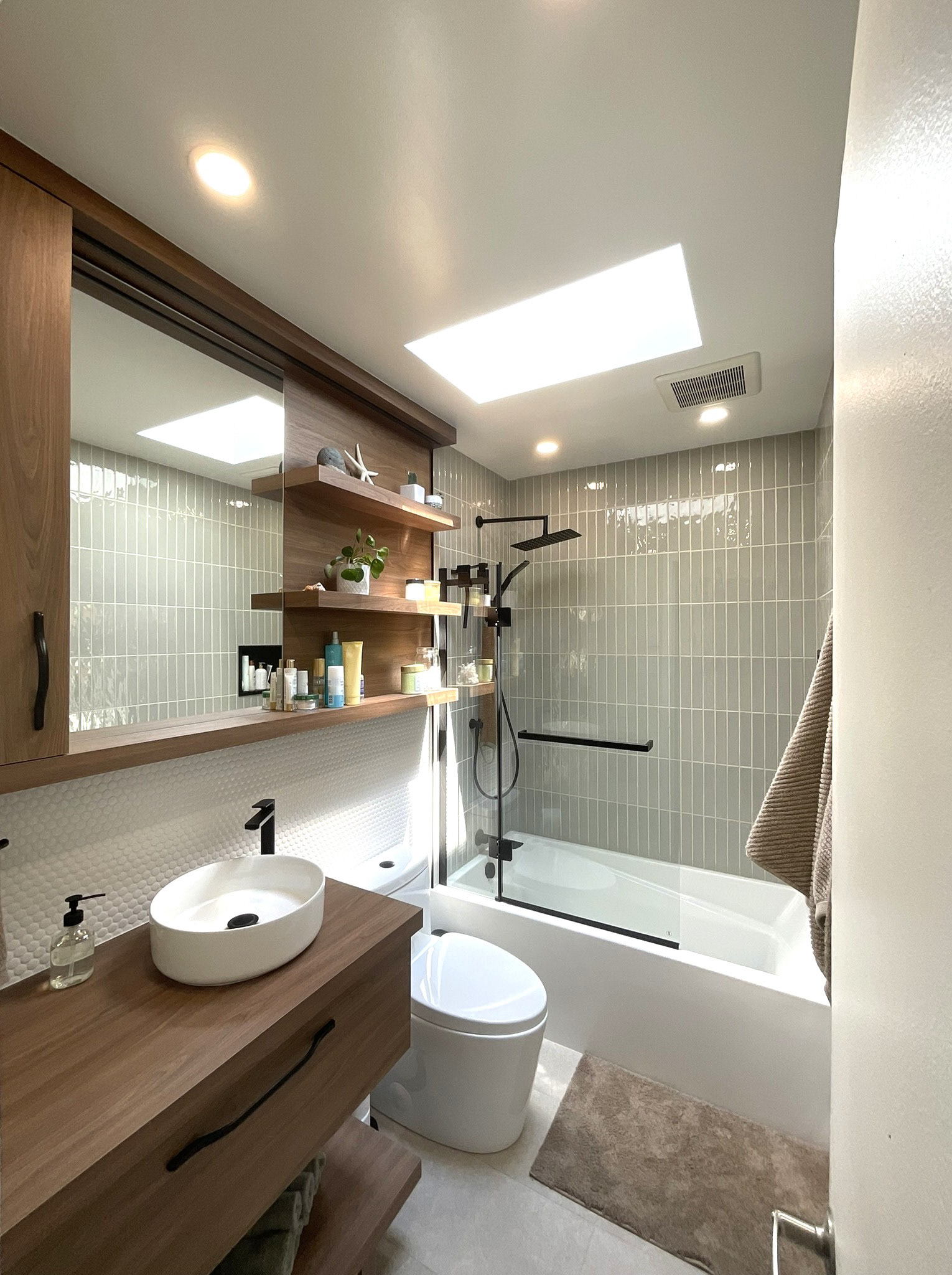 Rénovation complète d’une salle de bain compacte, transformée en espace chaleureux et relaxant. Les tons de sauge doux et le bois noyer naturel créent une atmosphère apaisante inspirée du spa, tandis que la robinetterie noire mate ajoute une touche moderne et élégante. L’éclairage naturel, les rangements sur mesure et les finis texturés contribuent à une ambiance de détente et de bien-être au quotidien.
