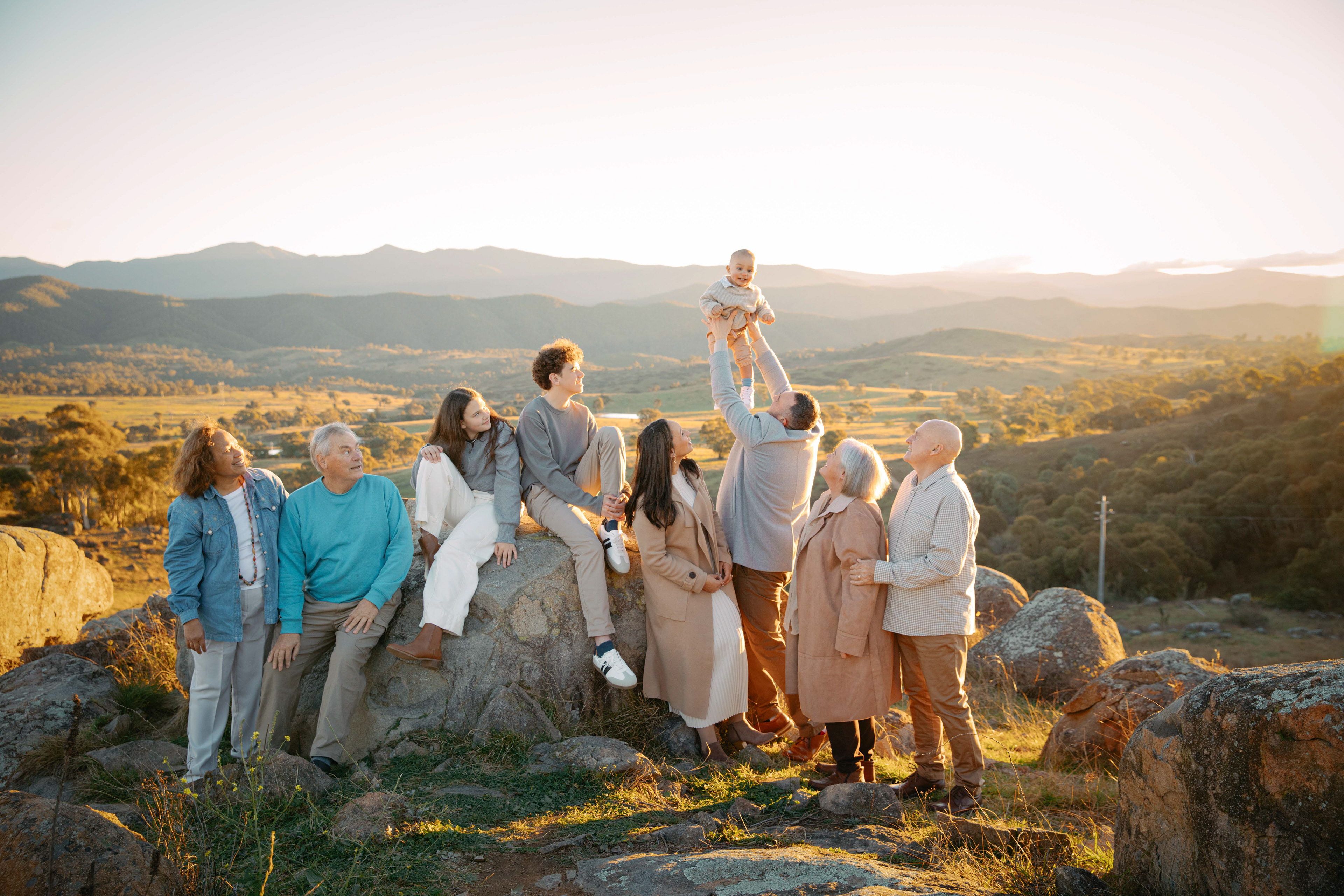 Three generations of family gathered outdoors at sunset, enjoying a golden hour portrait with mountain views.