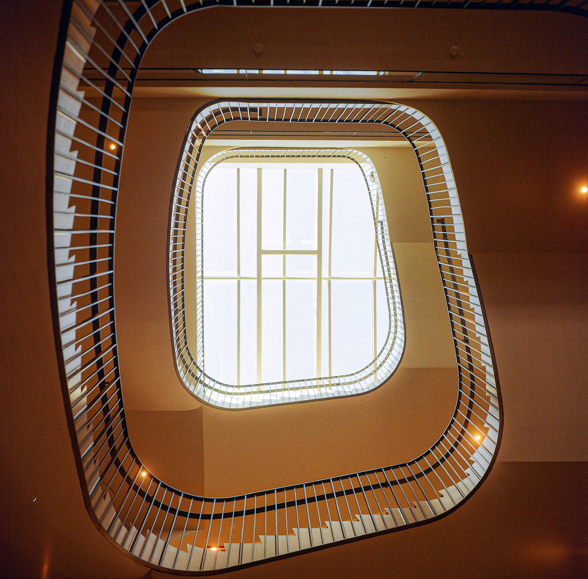 Interior architectural staircase with geometric skylight and curved lines illuminated by natural light. Explore the full series at dyoon.space.