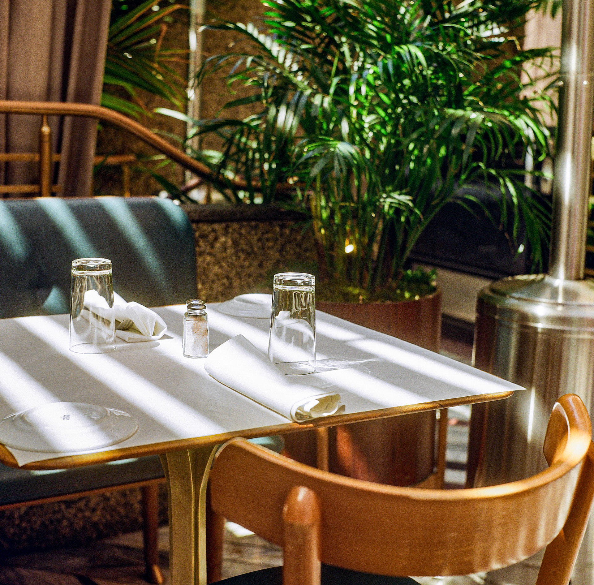 Sunlit restaurant interior with wooden furniture, soft shadows, and lush tropical greenery. Explore the full series at dyoon.space.