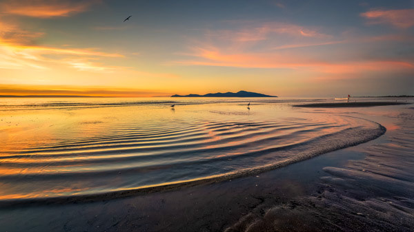 Kāpiti paddler: The end of a beautiful day as a paddler hauls their kayak out of the water and gentle waves ripple over the shore