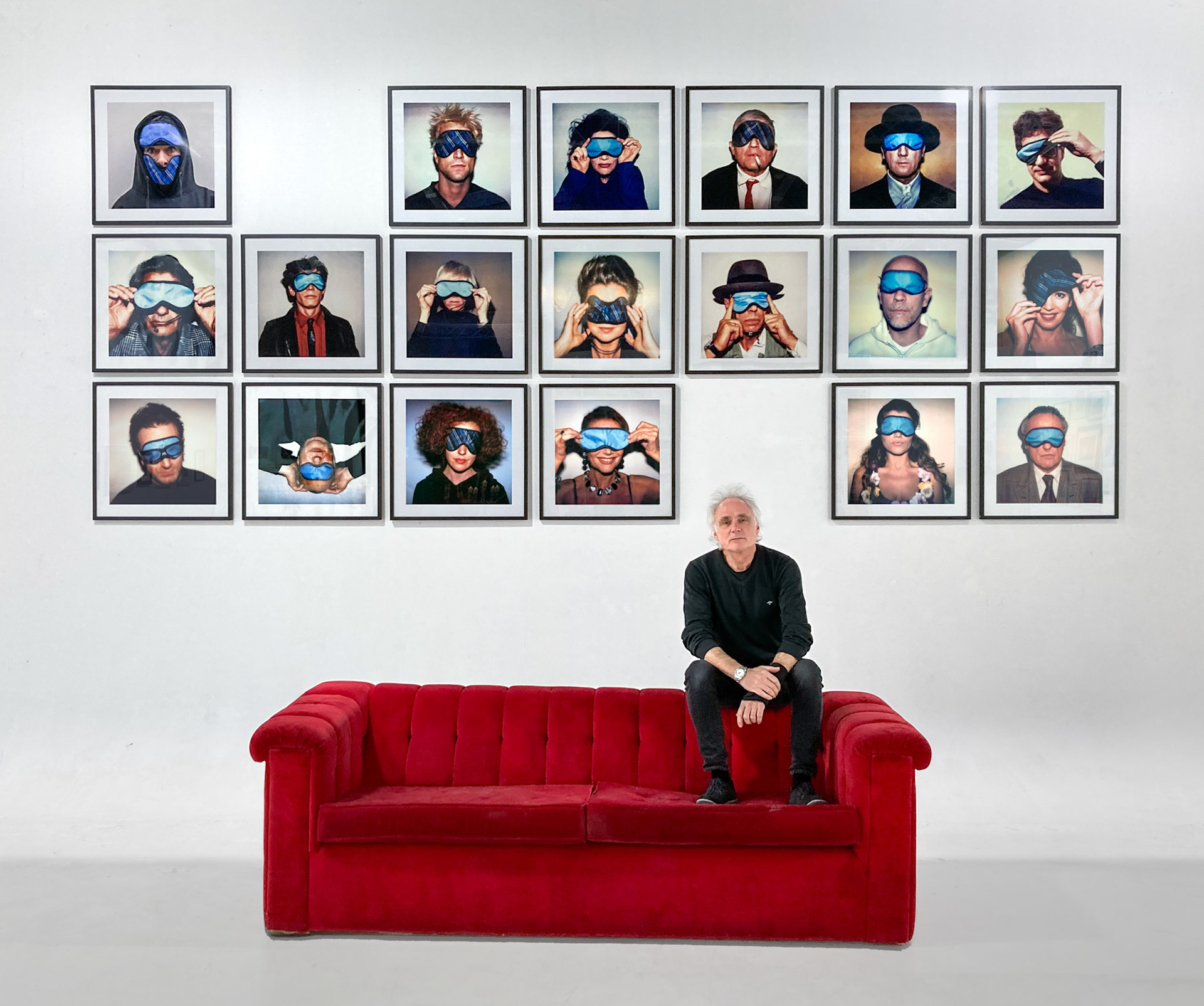 Freddy Langer sitzt auf Wackerbarths weltbekanntem rotem Sofa vor seiner Schlafmasken-Ausstellung im KUH Düsseldorf. Wieviele Weltstars erkennst du?